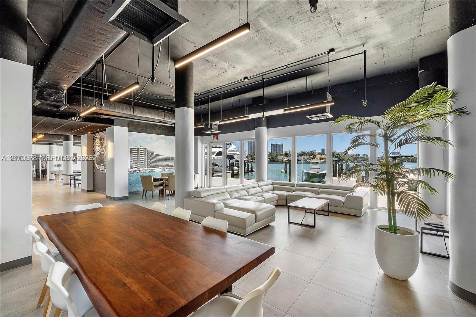 Open-concept living space featuring exposed concrete ceilings, industrial-style ductwork, floor-to-ceiling windows, ceramic tile flooring, and cylindrical structural columns