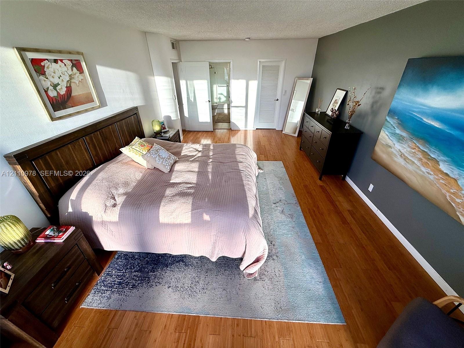 Bedroom featuring wood-finish flooring, a dark-toned accent wall, and two solid-core doors with louvered detailing