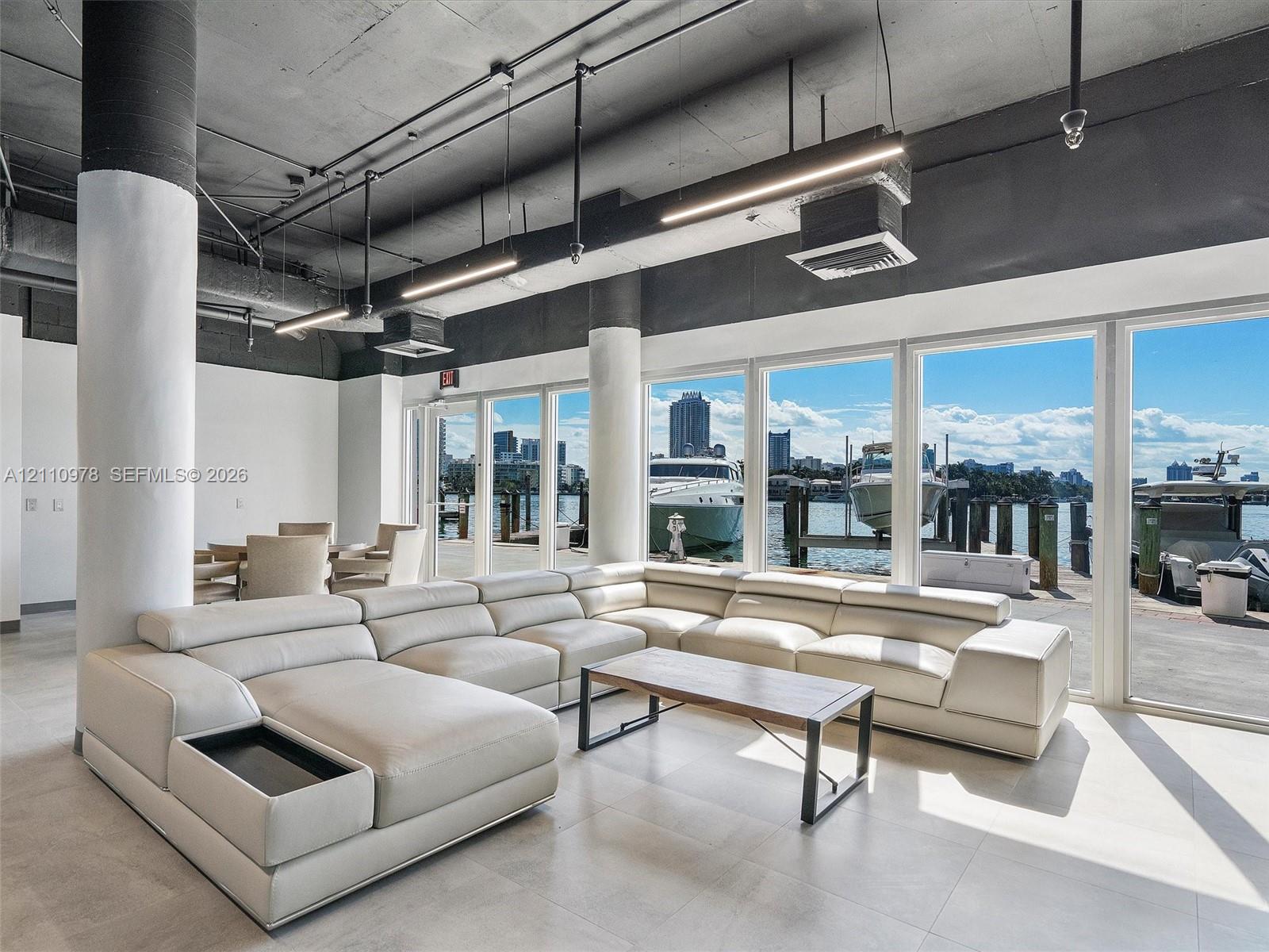 Industrial-style interior featuring exposed concrete ceilings, cylindrical structural columns, expansive floor-to-ceiling windows, and large-format tile flooring