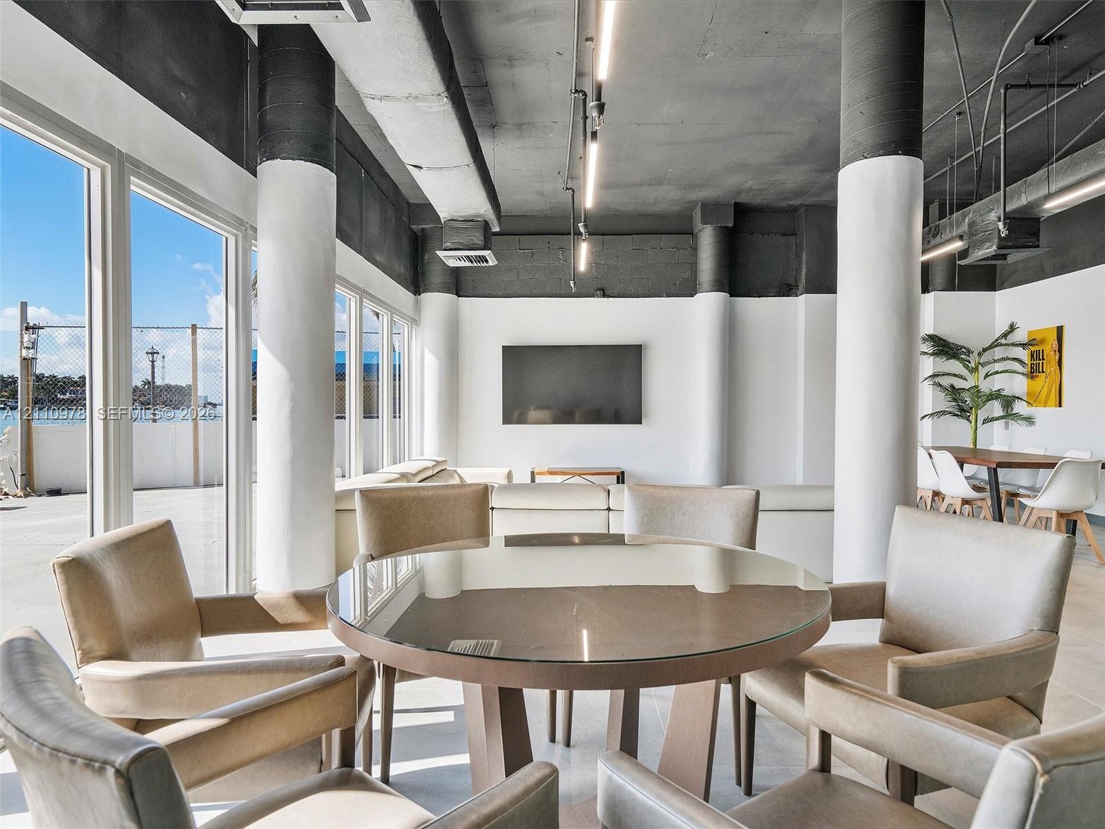 Industrial-style interior featuring high ceilings with exposed structural columns, floor-to-ceiling windows, polished concrete flooring, and linear track lighting