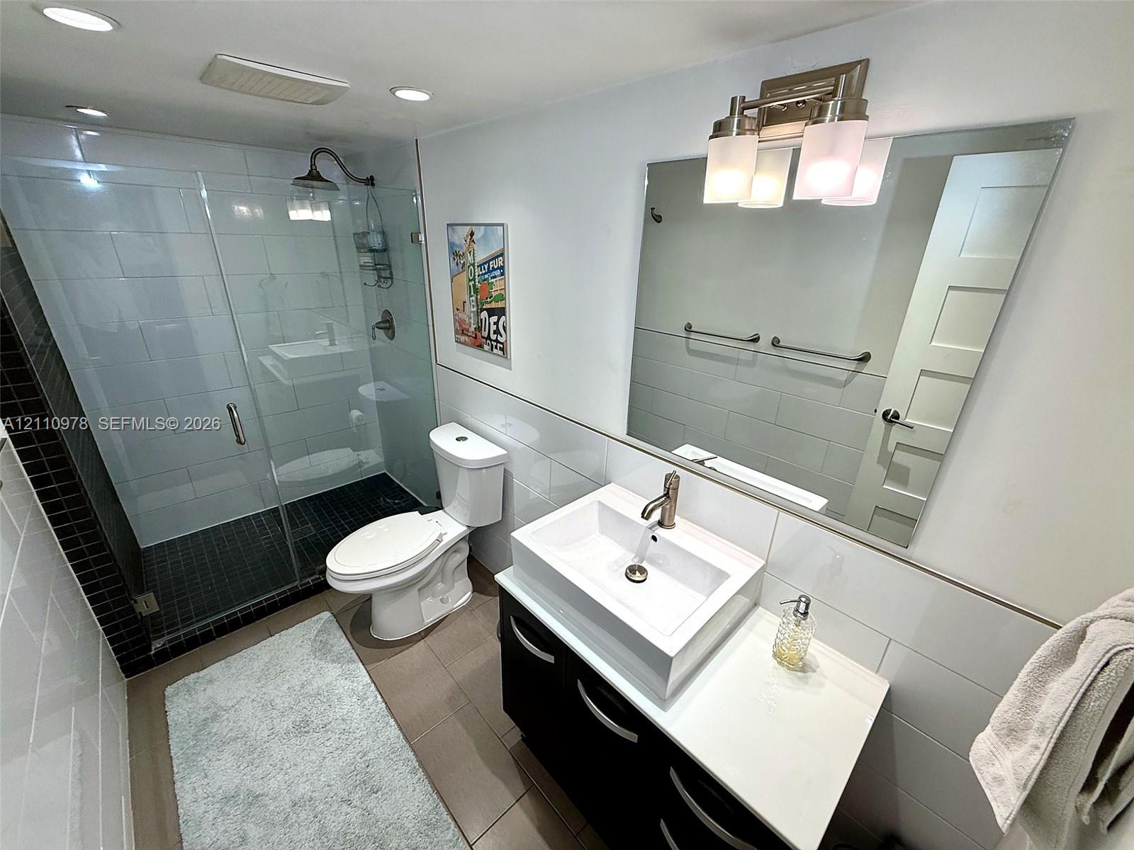 Bathroom featuring a glass-enclosed walk-in shower with tile surround, vanity with rectangular vessel sink, polished metal faucet, built-in cabinetry, and wall-mounted vanity lighting
