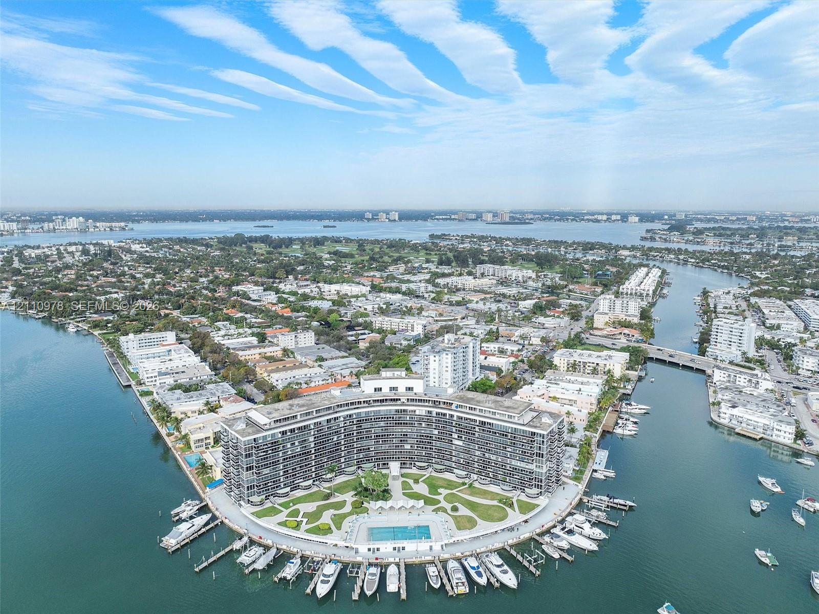 Waterfront high-rise building situated on a peninsula, featuring a swimming pool, manicured grounds, and private boat slips