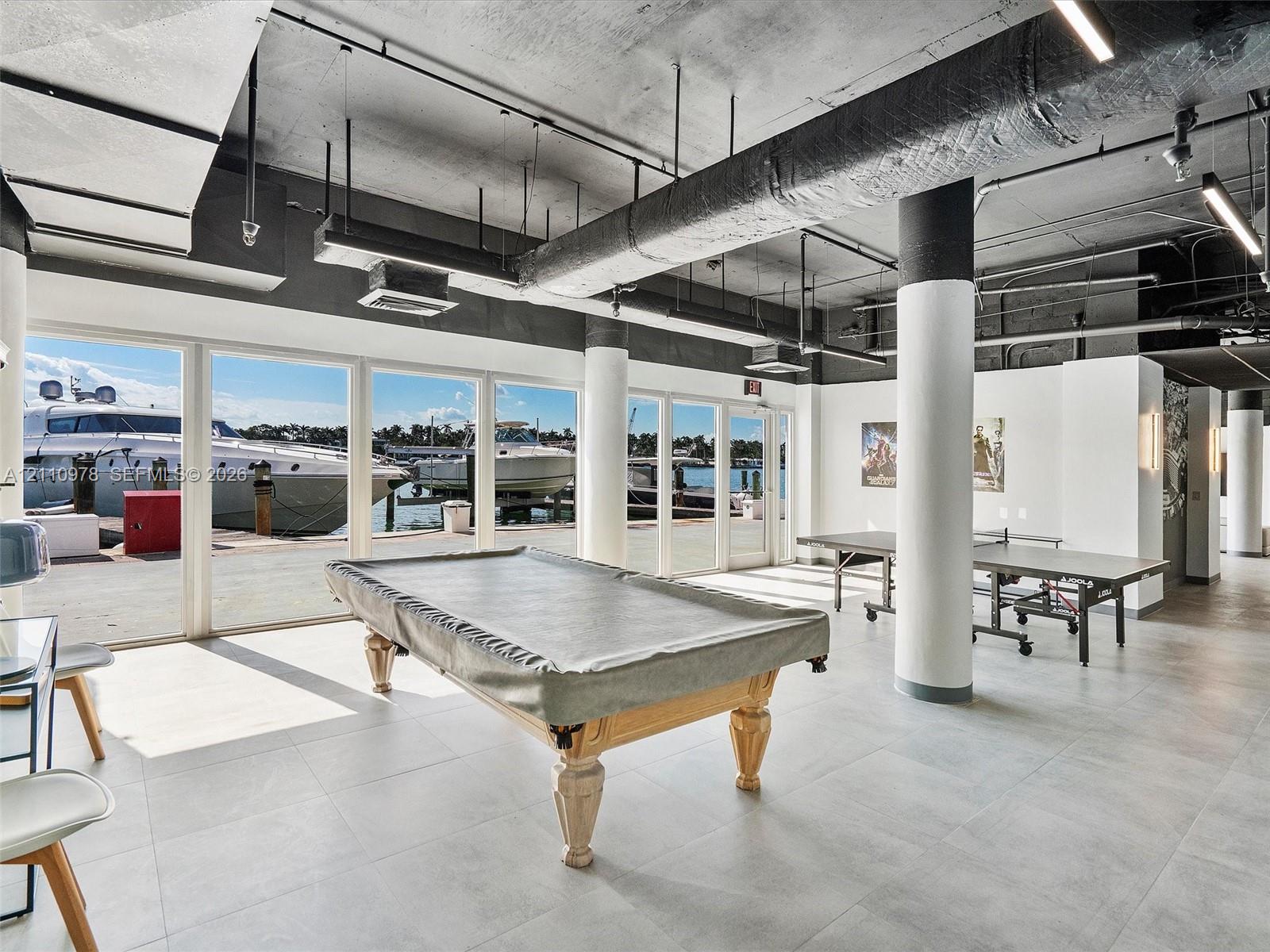 Industrial-style interior featuring a concrete ceiling with exposed ductwork, large-format tile flooring, floor-to-ceiling glass panel walls, and cylindrical structural columns