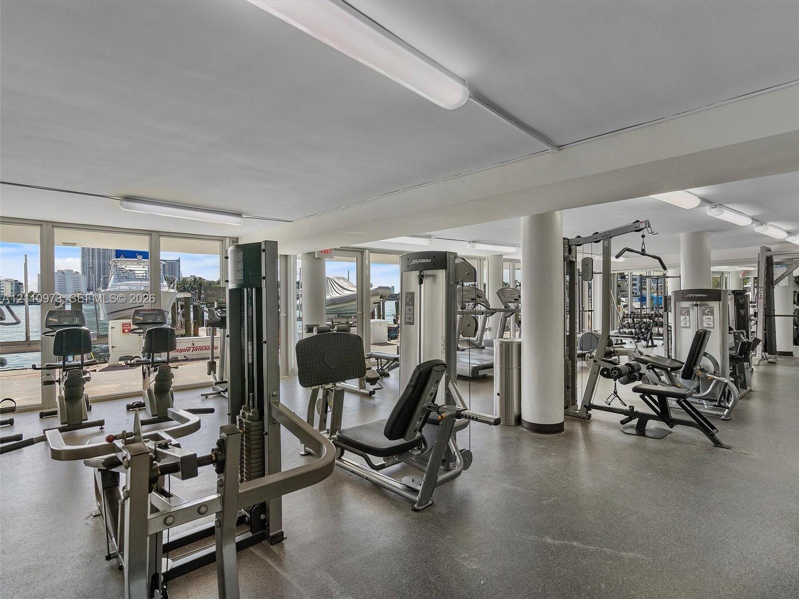 Fitness center featuring expansive floor-to-ceiling windows, polished concrete flooring, structural support columns, and recessed lighting