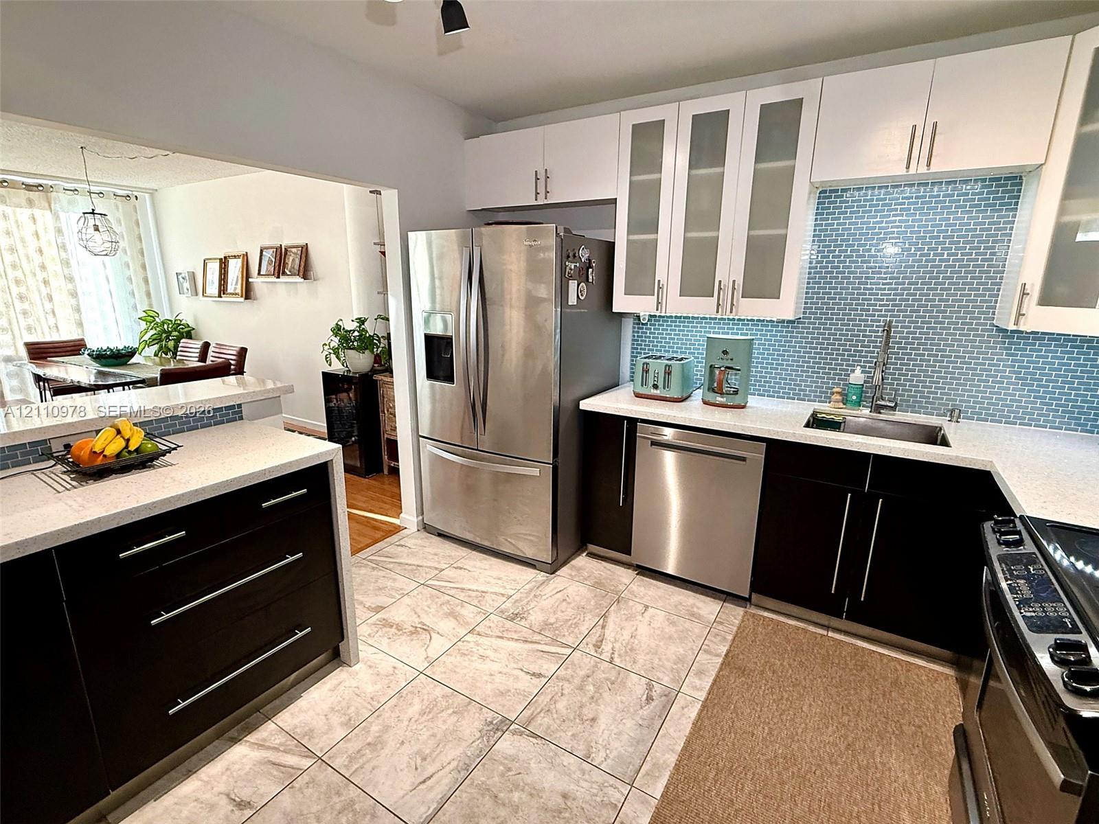 Kitchen featuring two-tone cabinetry, stainless steel appliances, quartz countertops, blue glass tile backsplash, and ceramic tile flooring