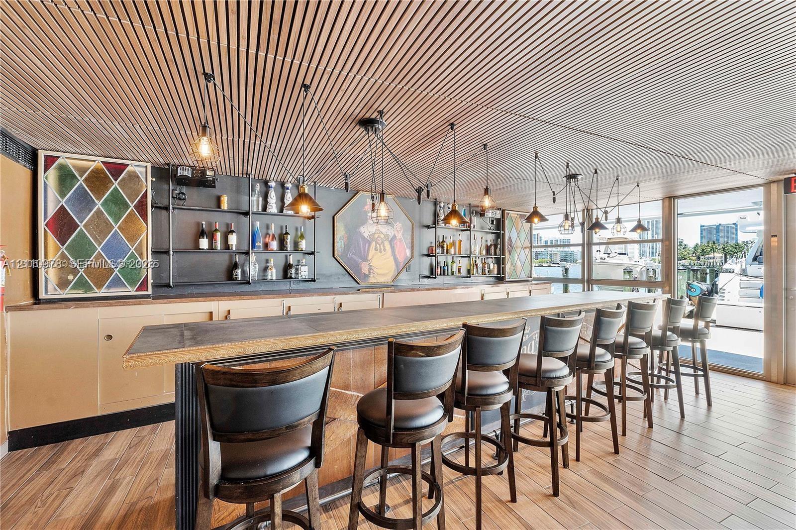 Built-in bar featuring a linear stone-finish countertop, wood-finish flooring, slatted wood ceiling, and black metal open-shelving cabinetry
