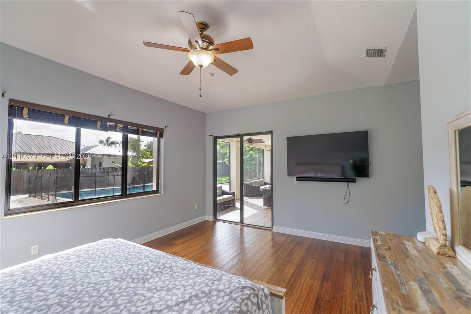 Wood-finish flooring, ceiling fan with integrated lighting, large picture window, and glass sliding door featuring access to a covered outdoor area