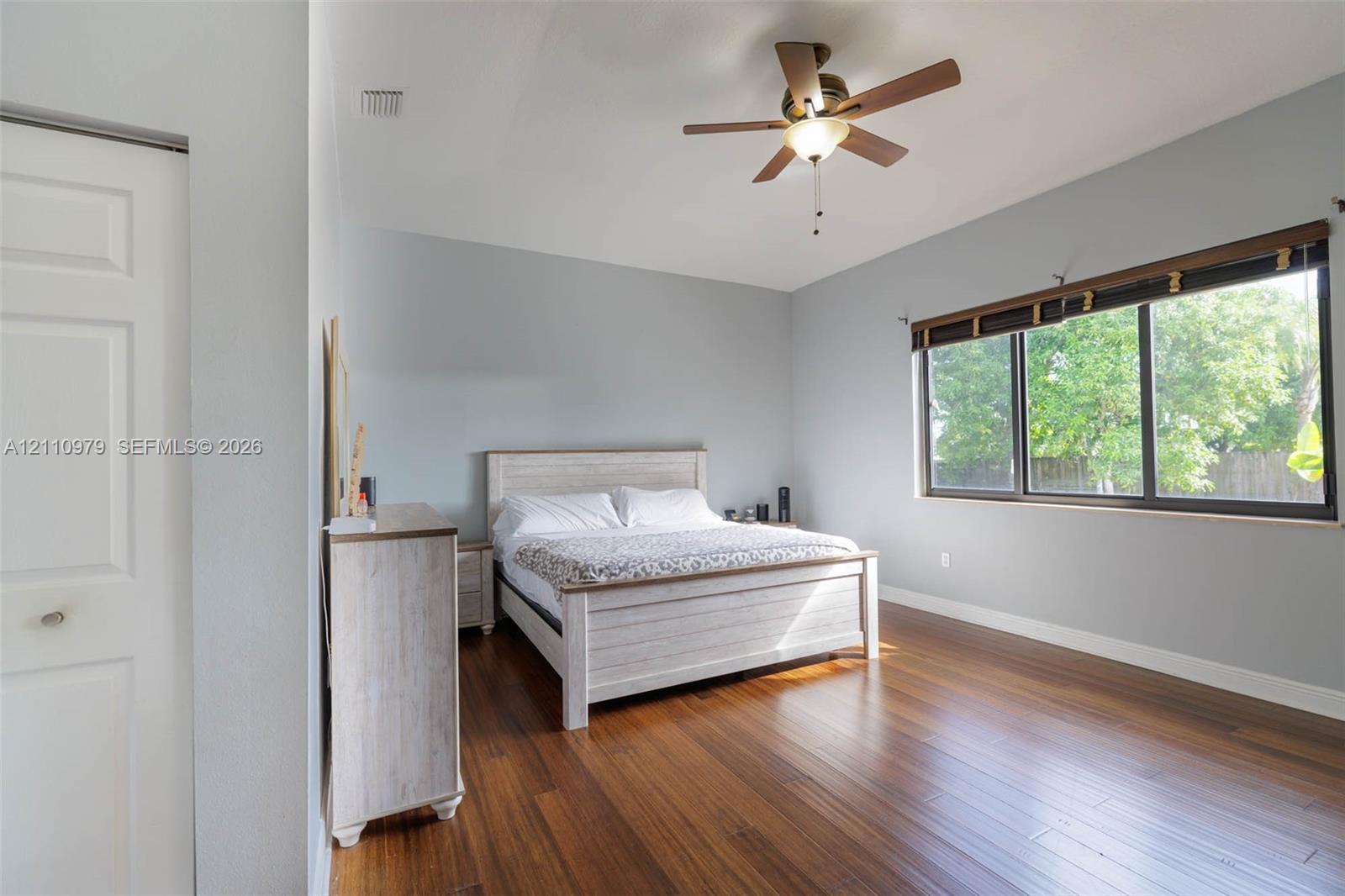 Spacious room featuring wood-finish flooring, a ceiling fan with integrated lighting, and large windows with dark-finish trim