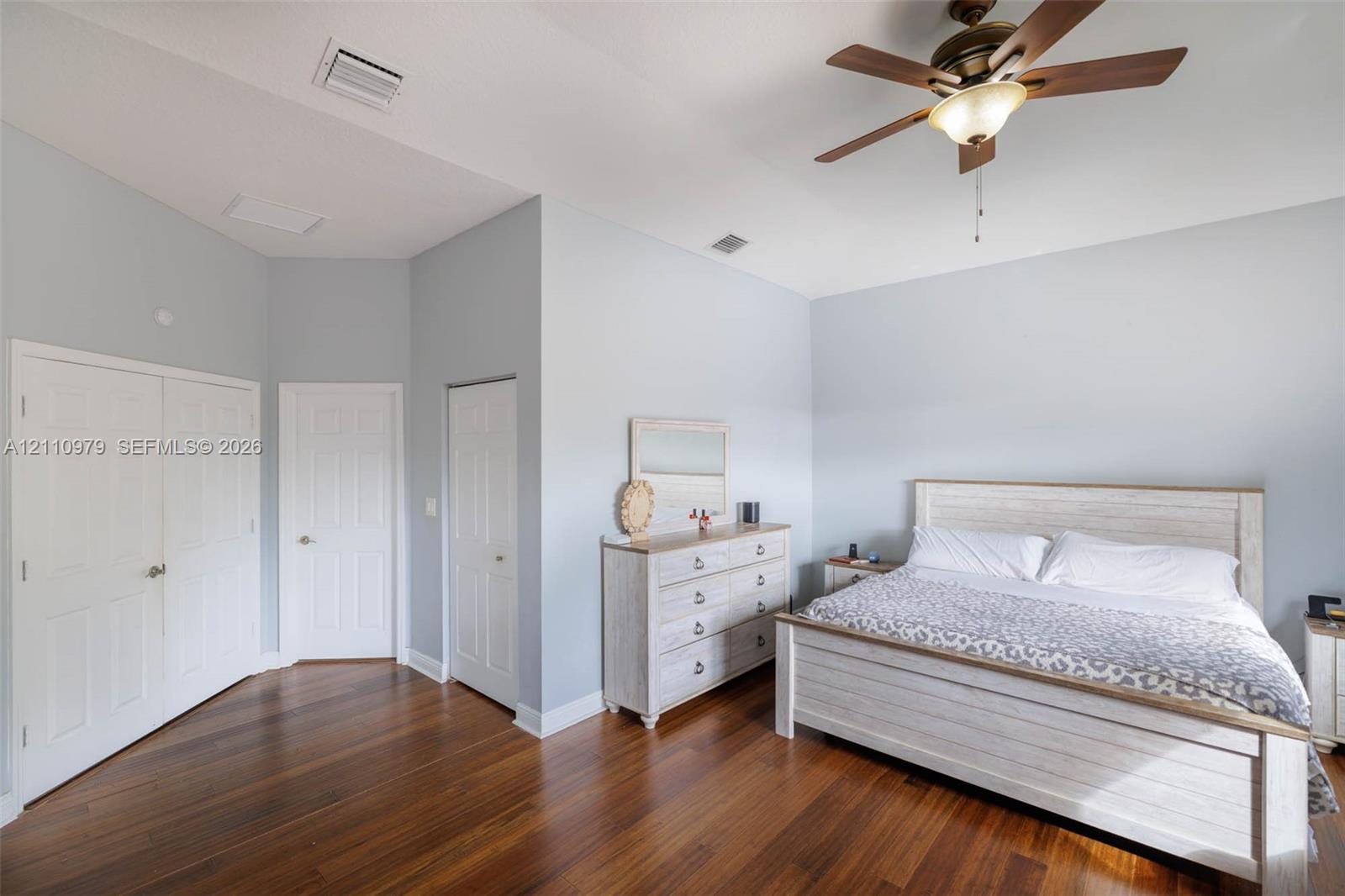 Vaulted ceiling featuring a central multi-blade ceiling fan with integrated lighting and high-gloss wood-finish flooring