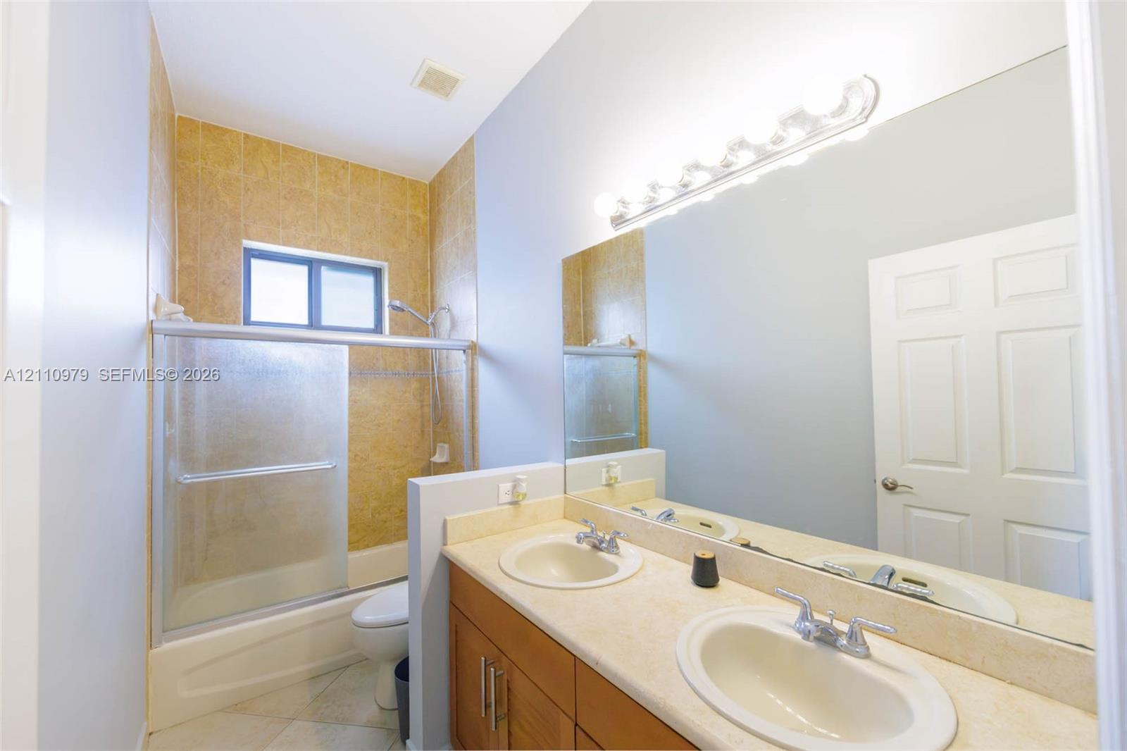Bathroom featuring a dual-sink vanity with solid-surface countertops, wood-finish cabinetry, a full-width wall mirror, and a tub-shower combination with tiled surround