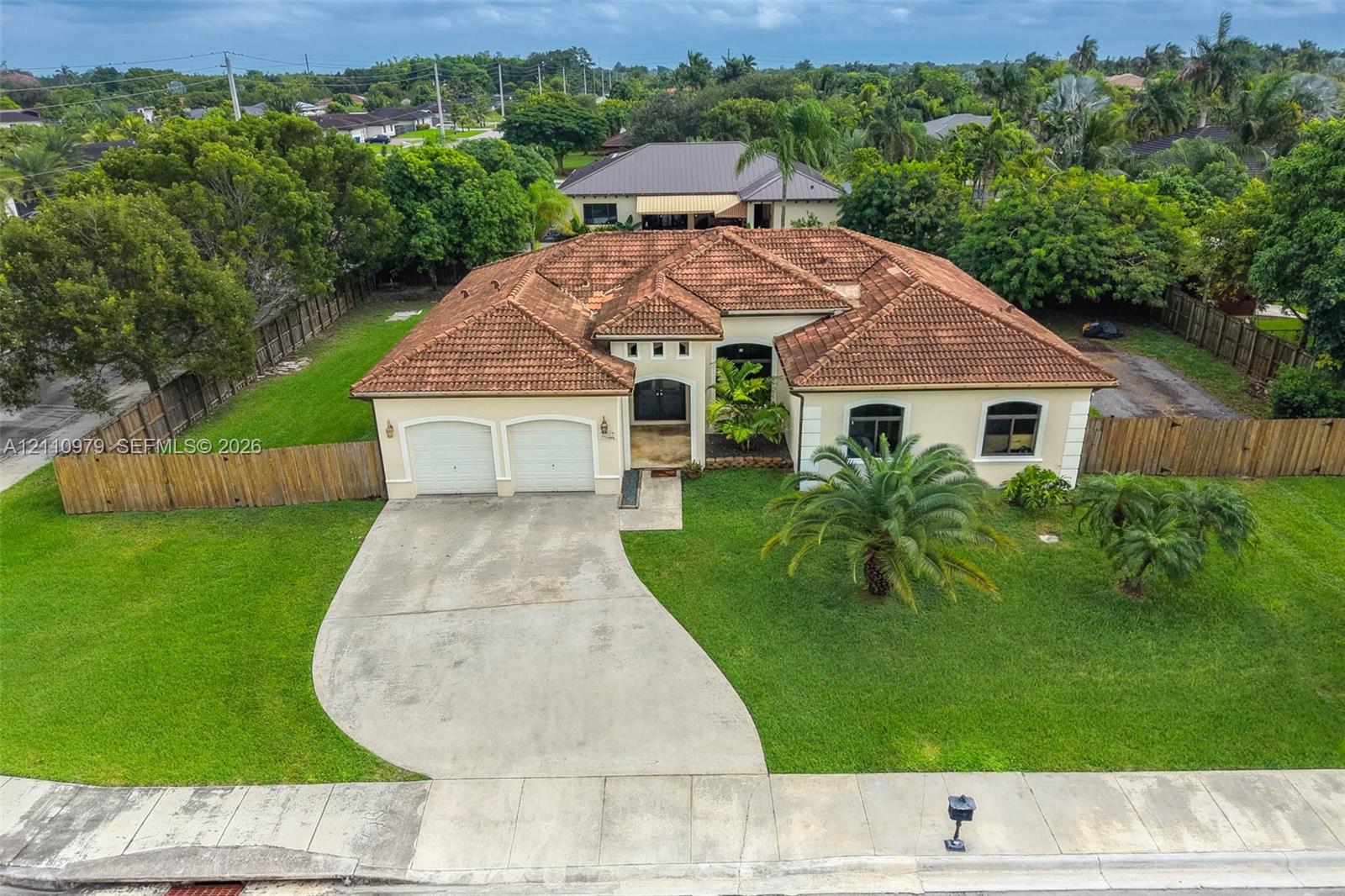 Single-story residence featuring a terracotta-tiled roof, stucco exterior, two-car garage, concrete driveway, and a fenced perimeter
