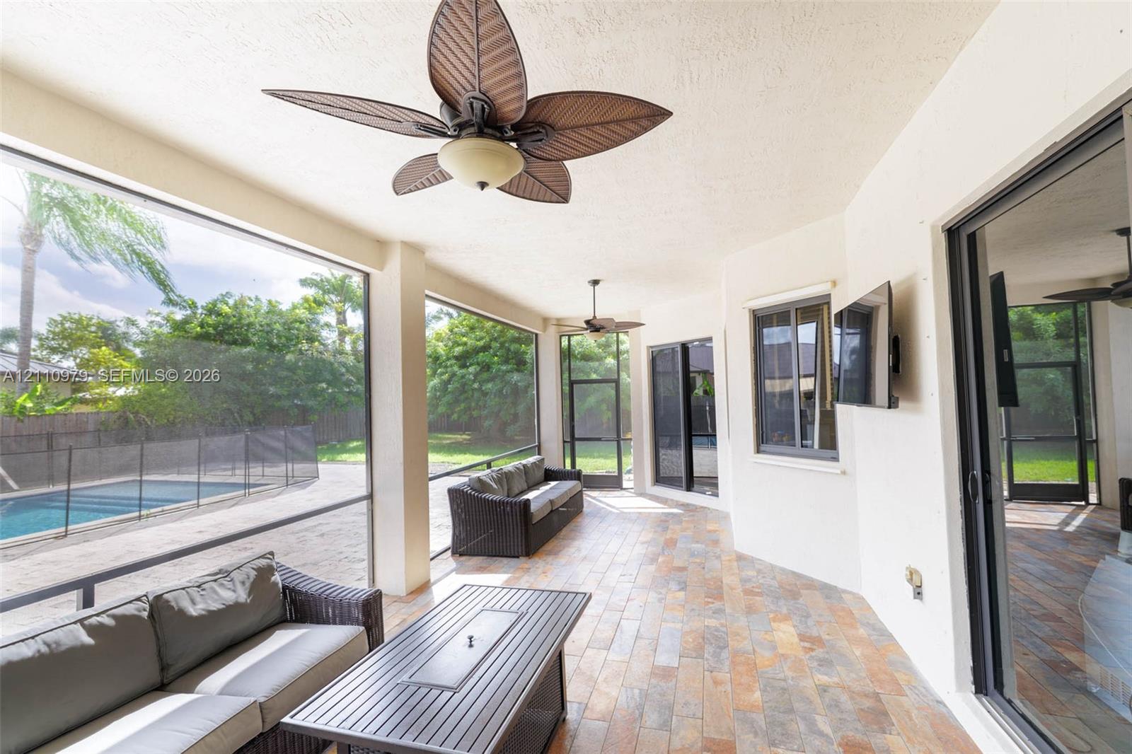 Screened-in lanai featuring tile flooring, ceiling fans, and an integrated pool area with security fencing
