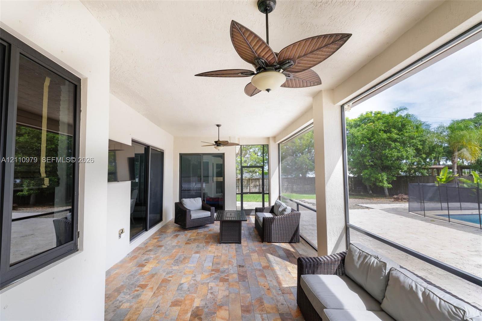 Screened lanai featuring multi-tonal stone flooring, ceiling fans, and dark-framed sliding glass doors