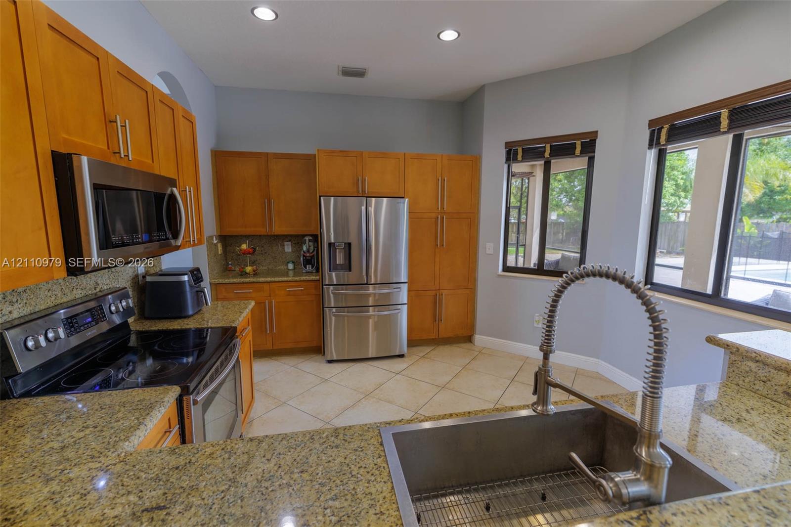 Kitchen featuring flat-panel wood cabinetry, stone countertops, stainless steel appliances, a deep undermount sink with a high-arch gooseneck faucet, and tiled flooring