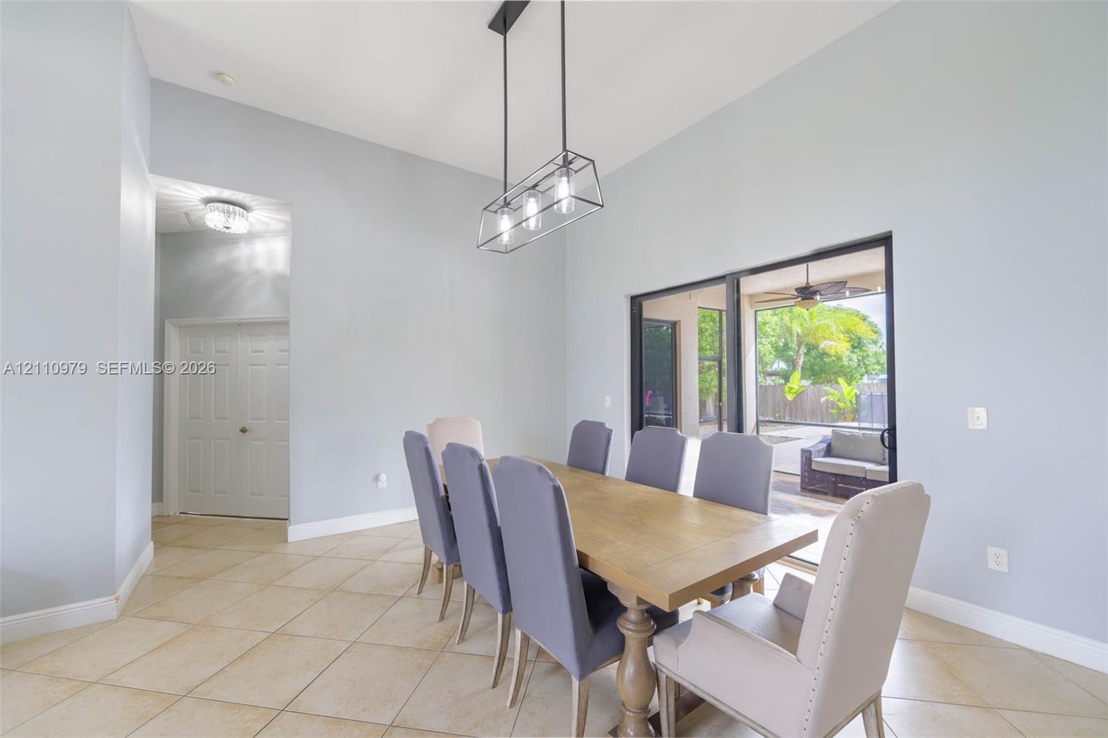High-ceiling interior featuring tile flooring, a rectangular metal-frame pendant light fixture, and sliding glass doors