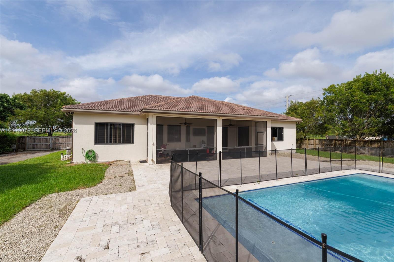 Rear elevation featuring a hip roof, screened-in lanai, paver patio, and in-ground pool with mesh security fencing