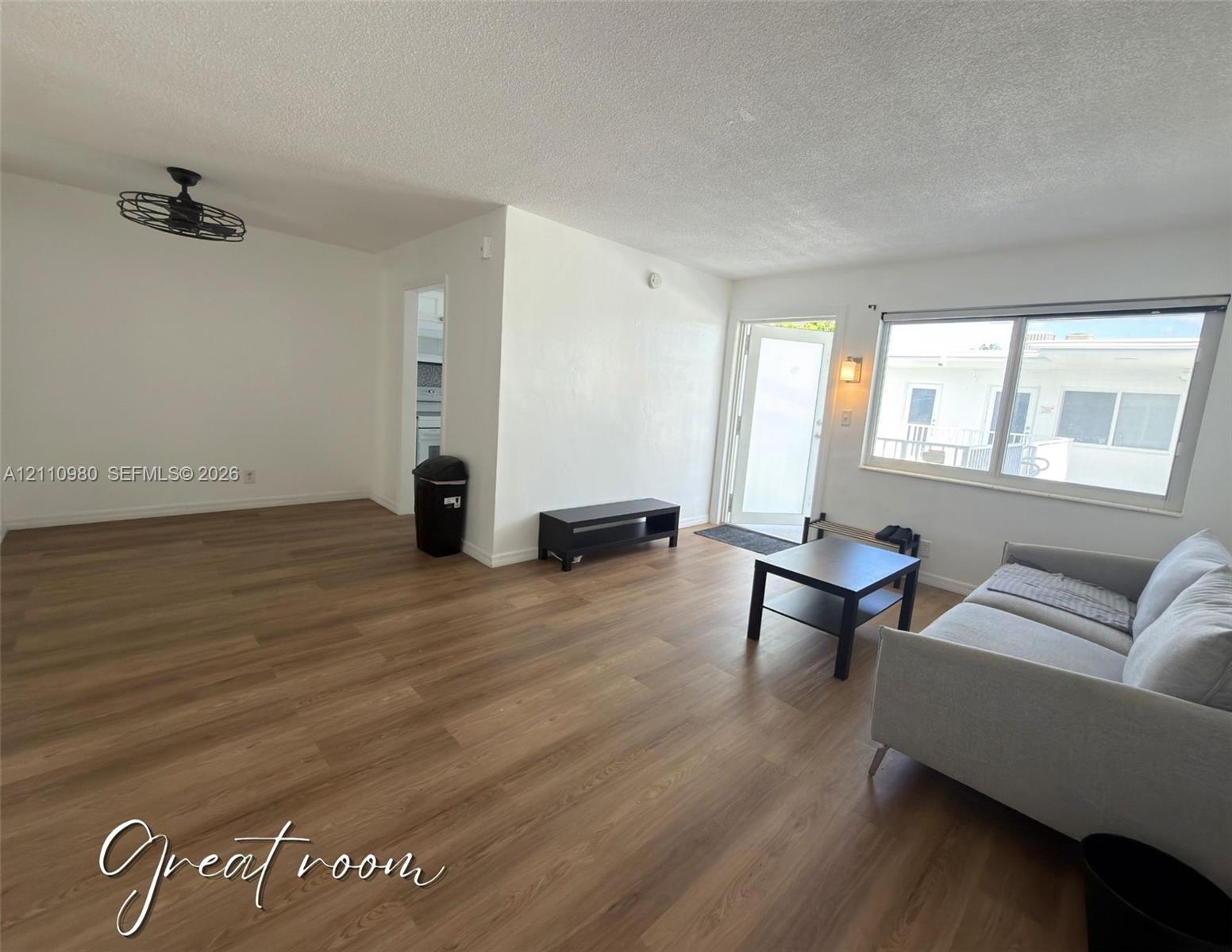 Open-concept space featuring wood-finish flooring, a large picture window, a matte black caged ceiling fan, and a neutral color palette