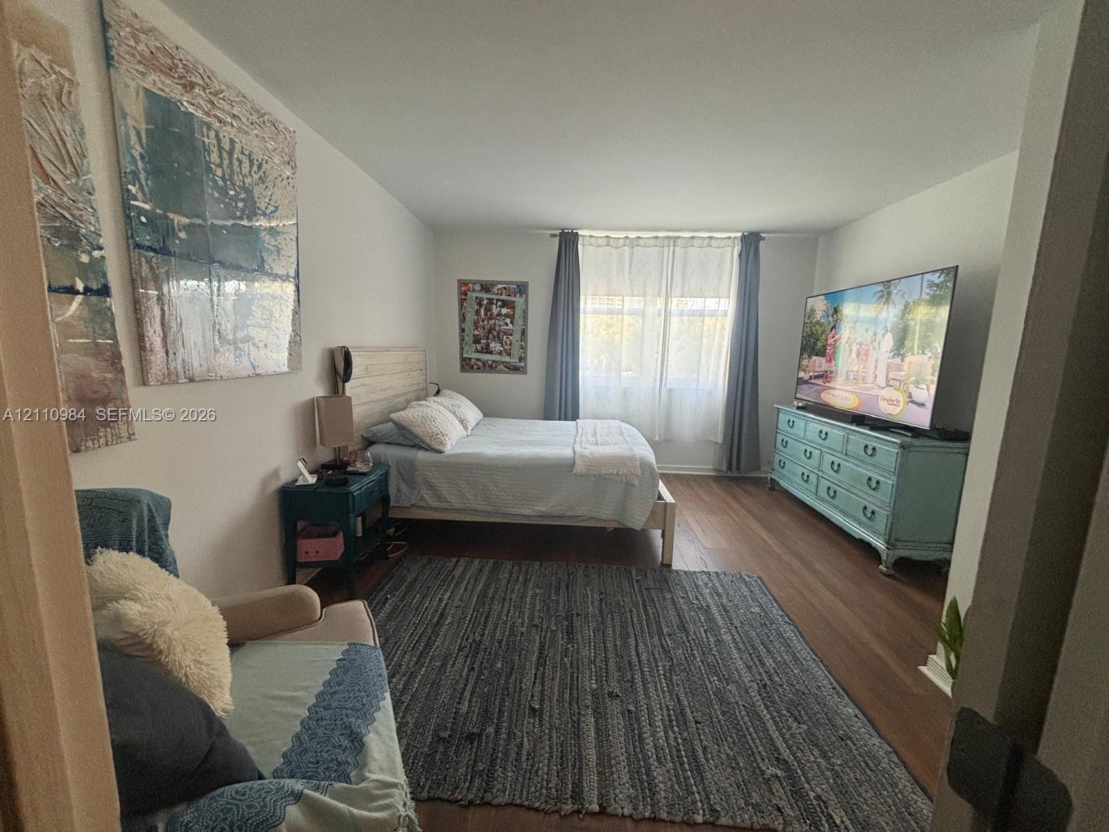 Bedroom featuring wood-finish flooring and a single window with curtain rods
