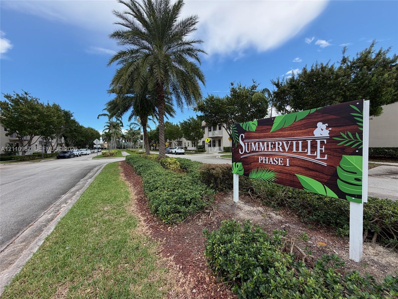Summerville Phase I community entrance featuring asphalt roadways, mature palm trees, landscaped shrubbery, and signage Summerville Phase I community entrance featuring asphalt roadways, mature palm trees, landscaped shrubbery, and signage