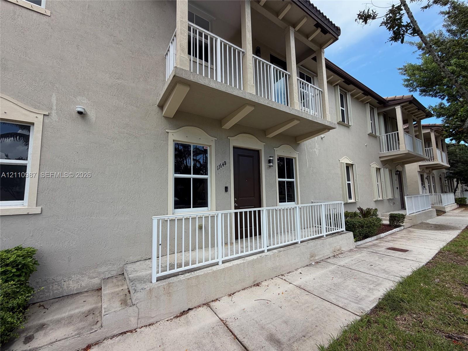 Stucco exterior featuring a second-story balcony with metal railing, raised concrete porch with matching metal railing, and decorative window molding