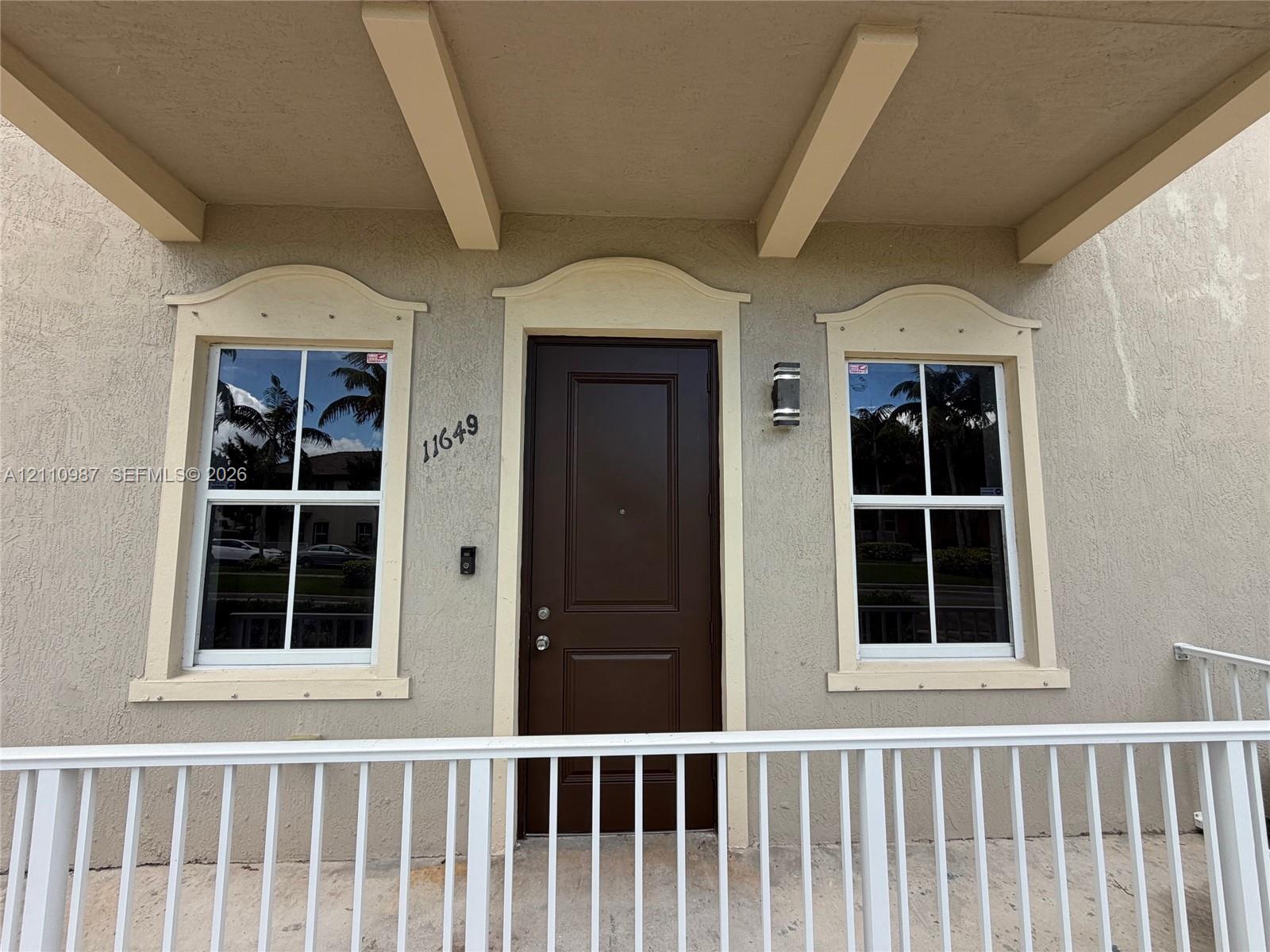 Covered entryway featuring a solid-panel door, decorative window pediments, and a white metal railing