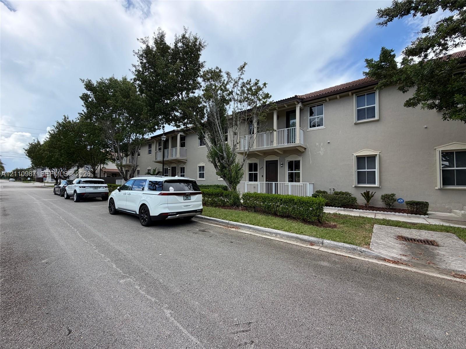 Two-story stucco exterior featuring covered balconies, recessed entryways, tile roof, and manicured shrubbery