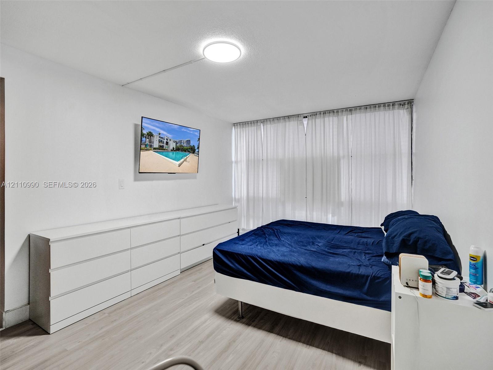 Light-toned wood-finish flooring, floor-to-ceiling sheer window treatments, and a flush-mount ceiling light fixture