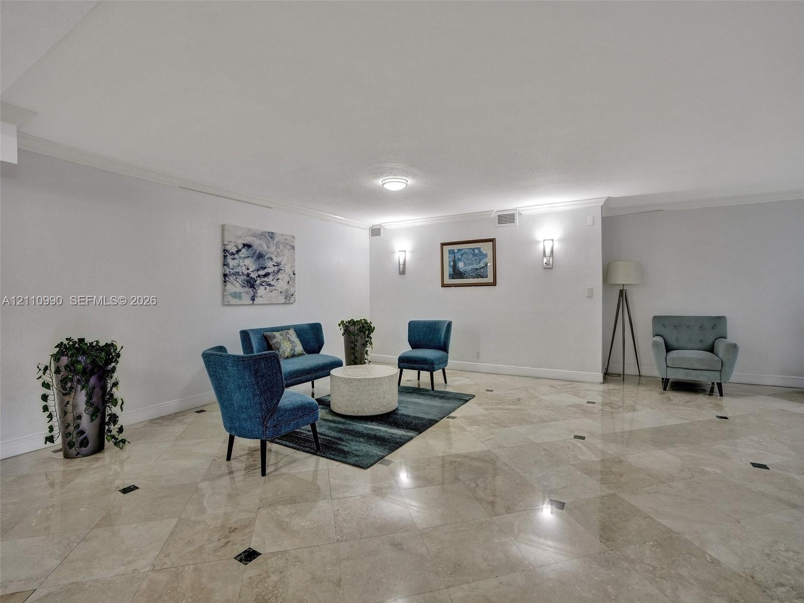 Polished stone flooring with decorative inset accents, crown molding, and wall-mounted light fixtures