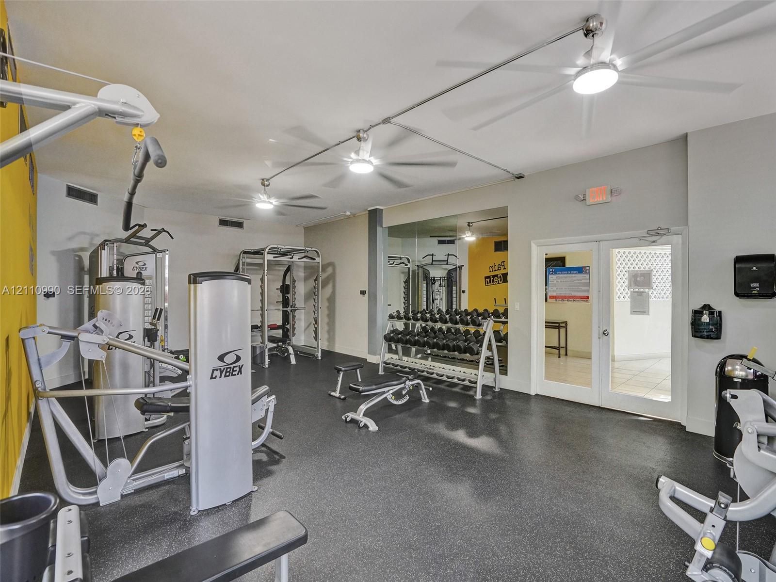 Fitness area featuring durable rubber flooring, mirrored walls, and multiple ceiling-mounted fans
