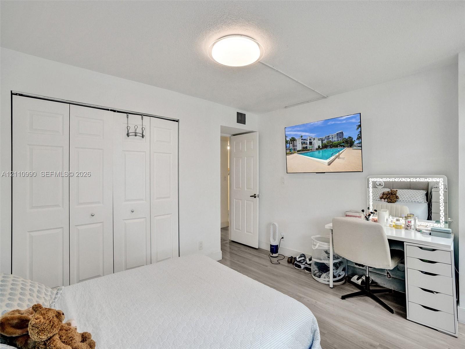 Light-filled room featuring wood-finish flooring, a wall-mounted television, and a four-panel bi-fold closet