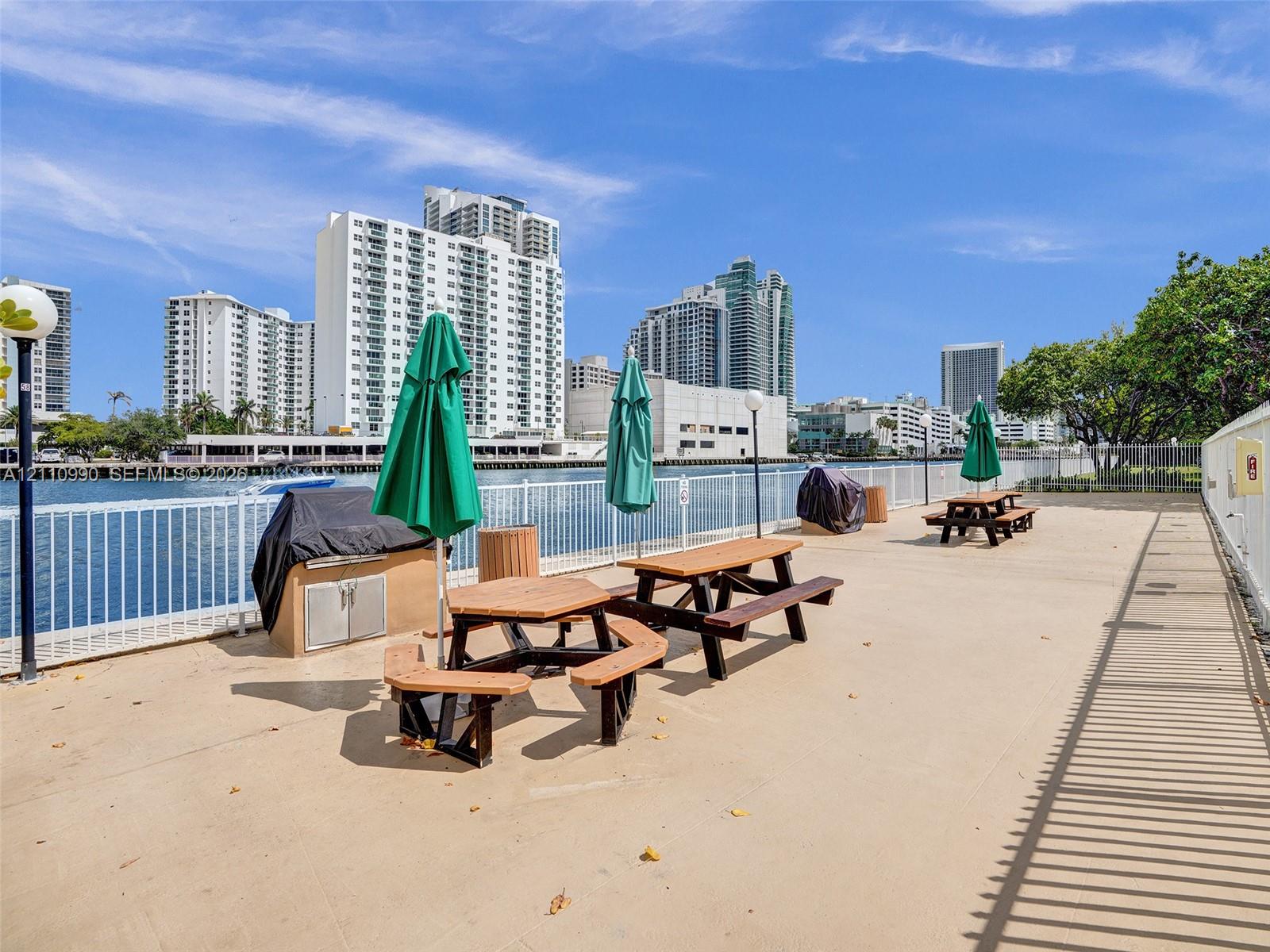 Waterfront terrace featuring a concrete deck, metal perimeter fencing, built-in stainless steel grilling station, and pole-mounted outdoor lighting