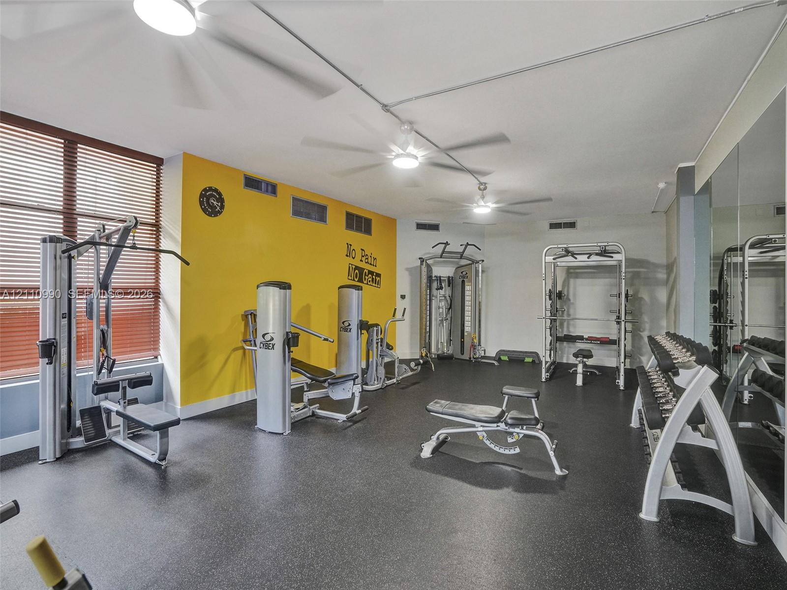 Fitness room featuring durable rubber flooring, mirrored walls, and multiple ceiling-mounted fans