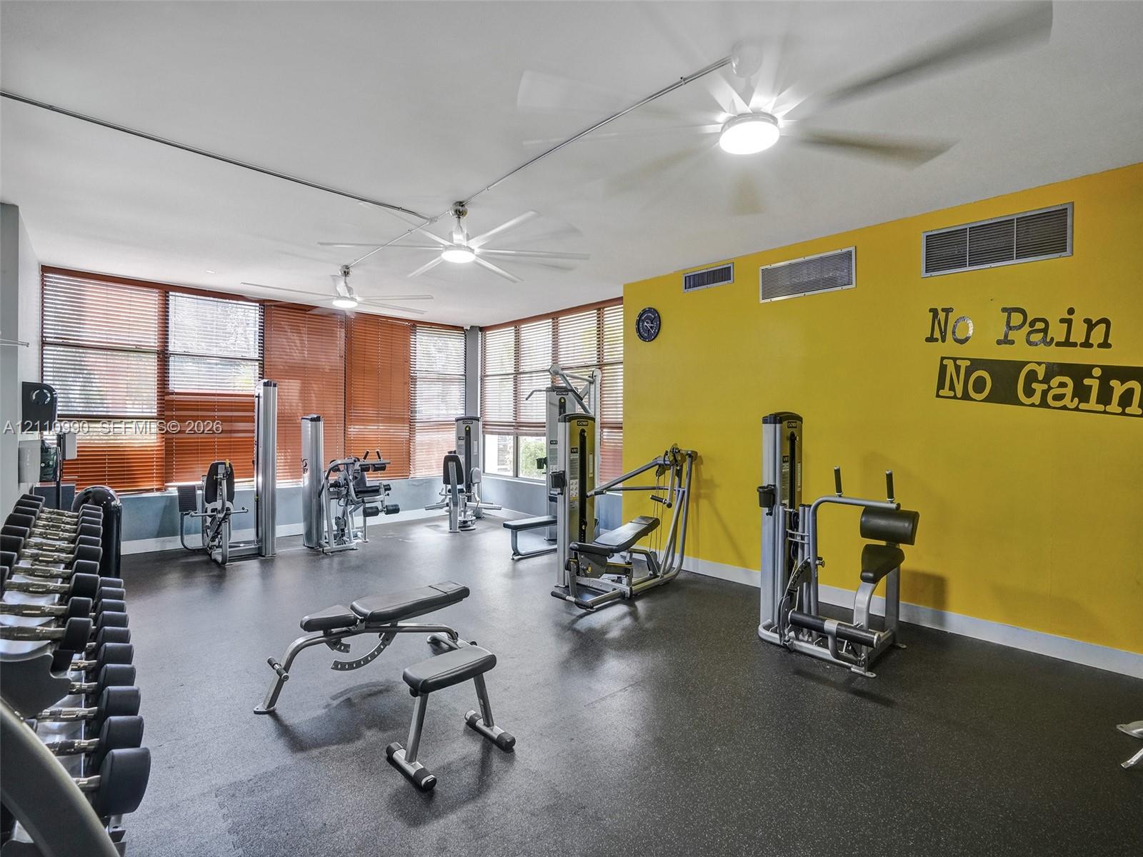 Fitness space featuring rubberized flooring, expansive windows with integrated blinds, and multiple ceiling-mounted light fixtures