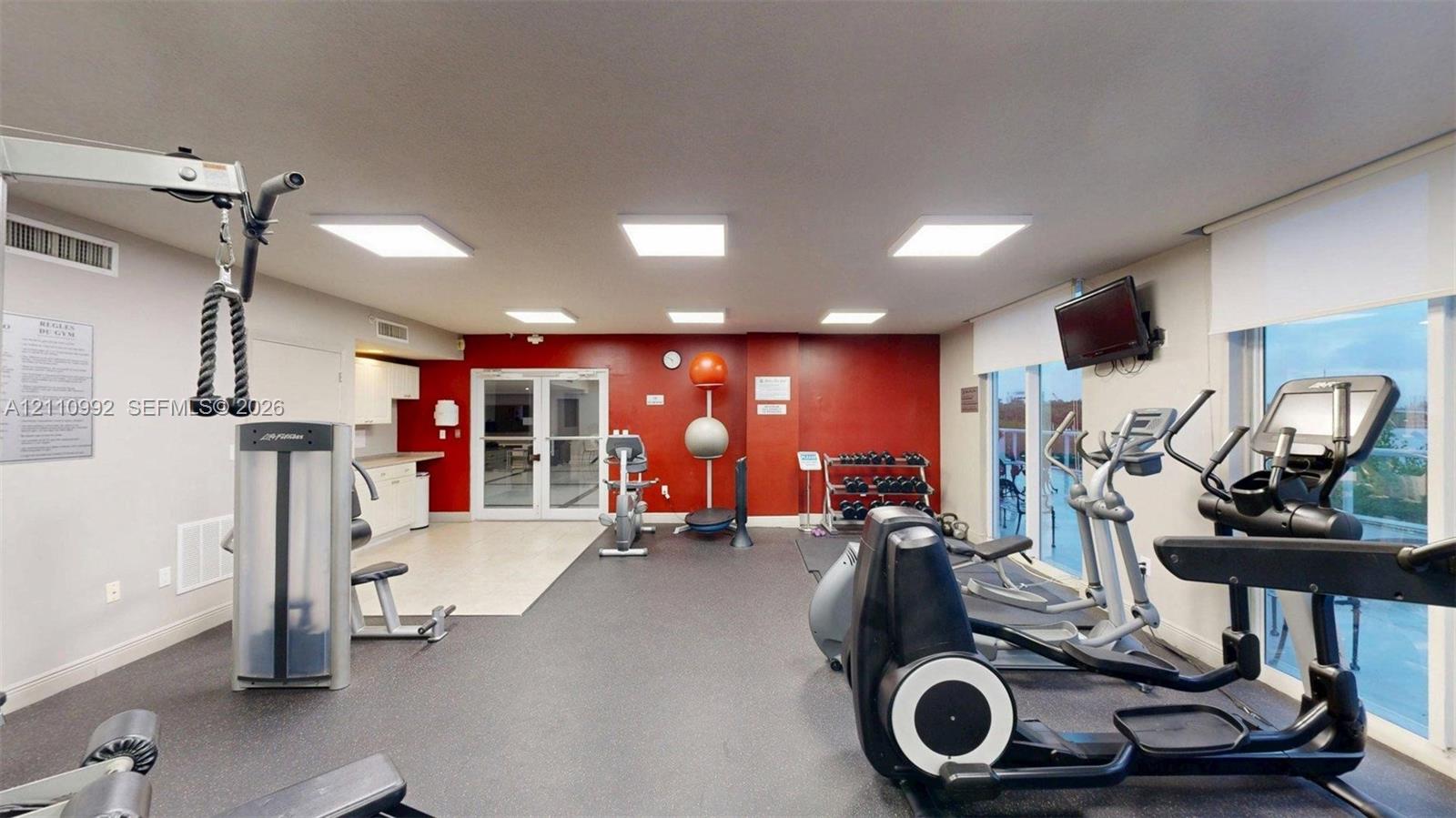 Fitness facility featuring recessed LED lighting, durable rubber flooring, glass-paneled entry doors, and expansive floor-to-ceiling windows