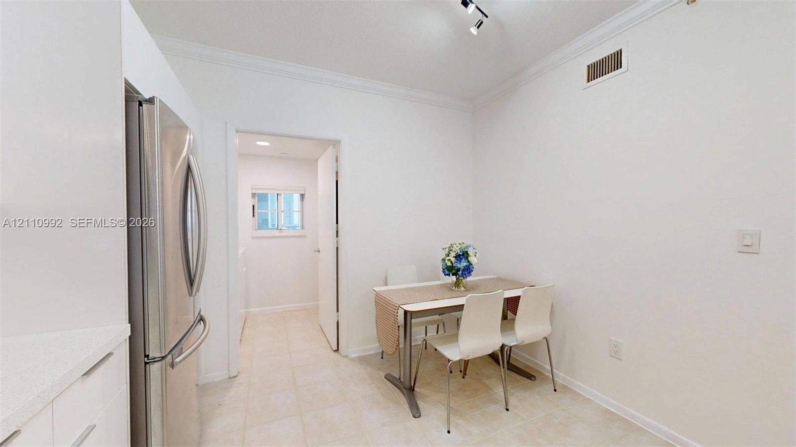 Stainless steel refrigerator, neutral tile flooring, crown molding, and multi-directional track lighting