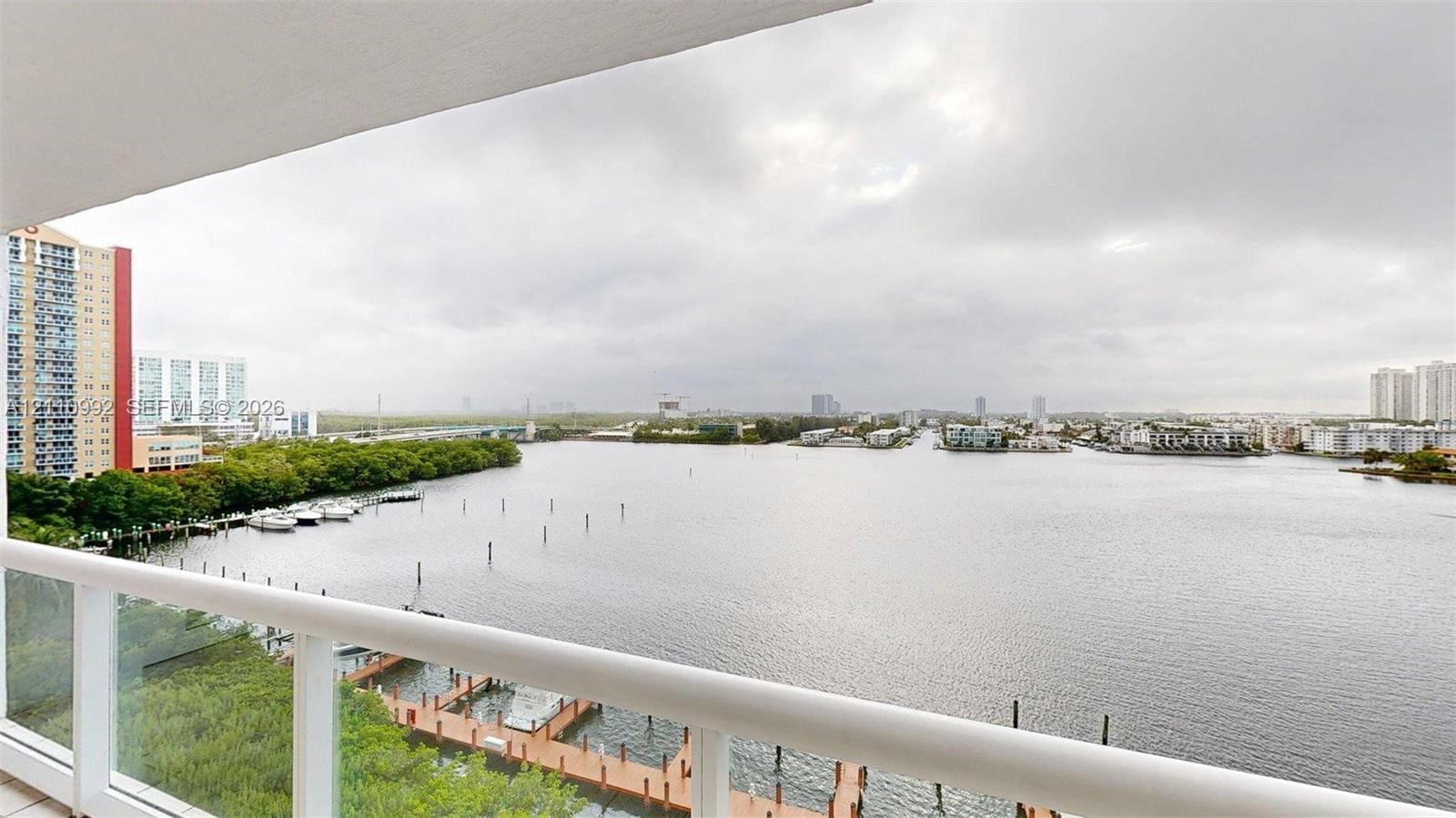 Balcony featuring a white railing with glass panels, overlooking a waterway with private boat docks