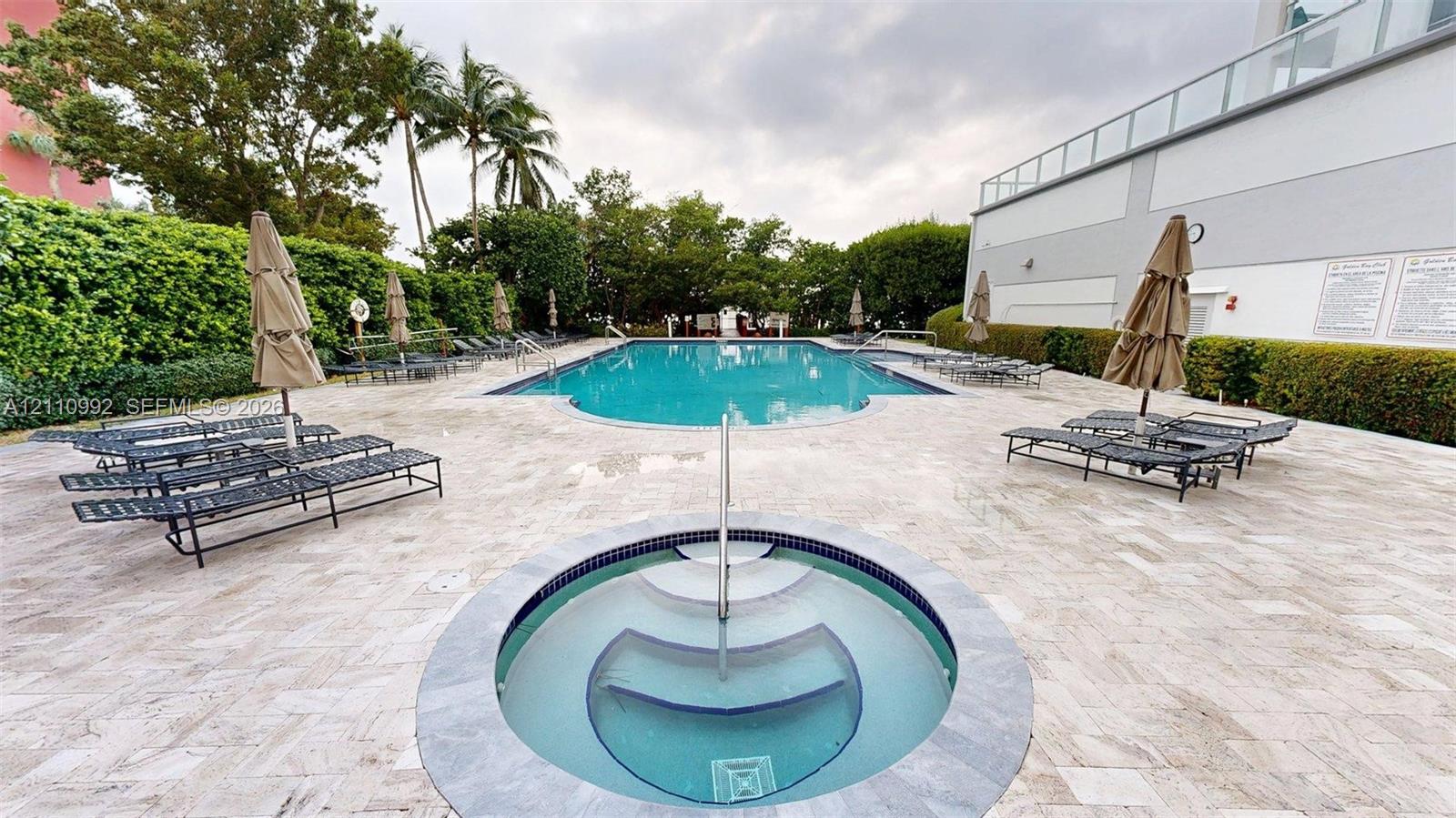 Outdoor swimming pool and spa featuring stone-tiled decking, a stainless steel handrail, and perimeter privacy hedging