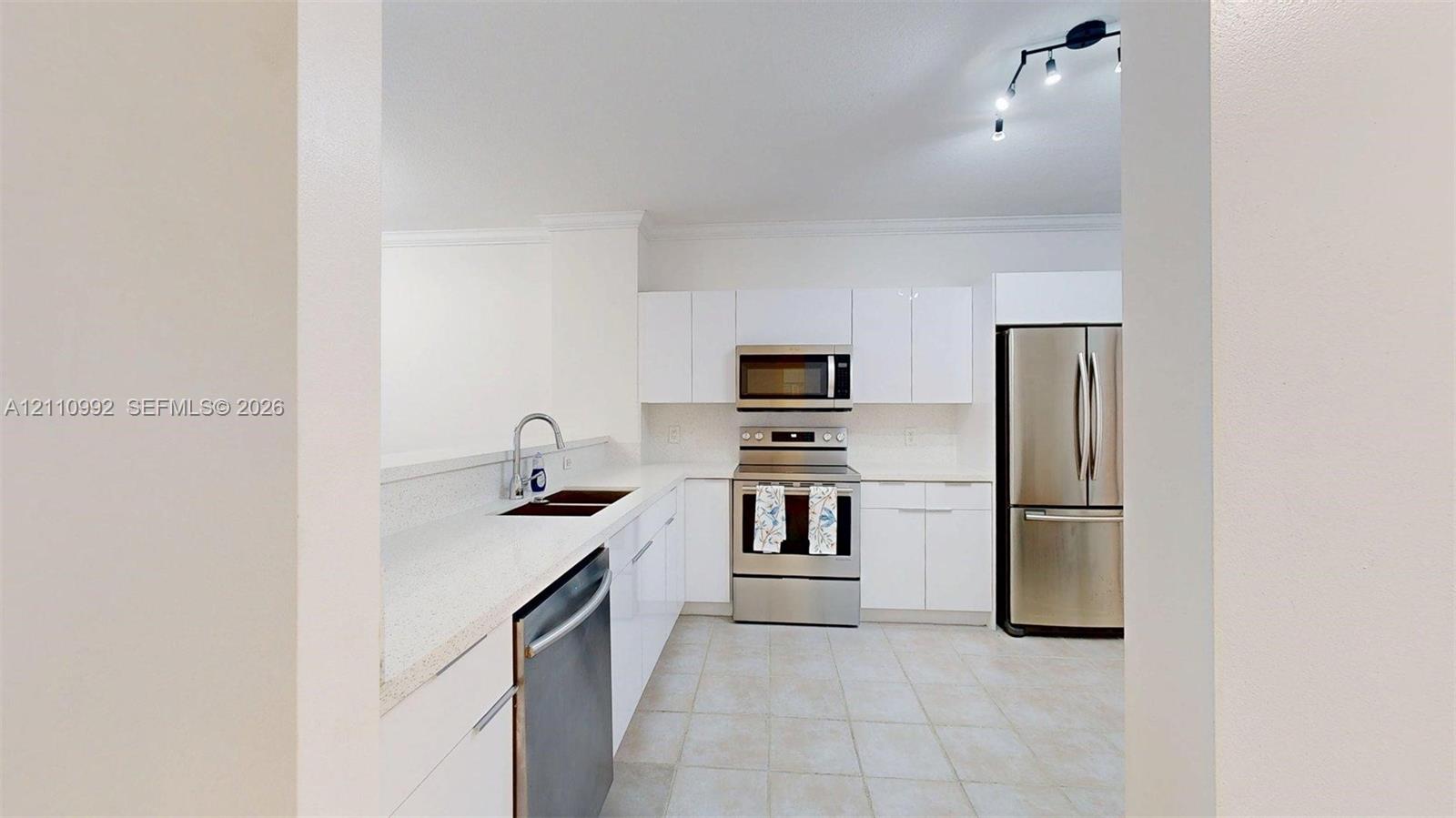 Kitchen featuring white slab cabinetry, stainless steel appliances, solid-surface countertops, dual-basin undermount sink, and tile flooring