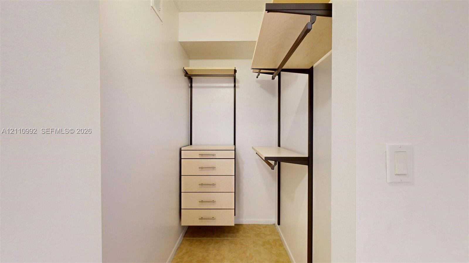 Walk-in closet featuring light-toned custom shelving, a built-in five-drawer chest, and dark metal hardware finishes