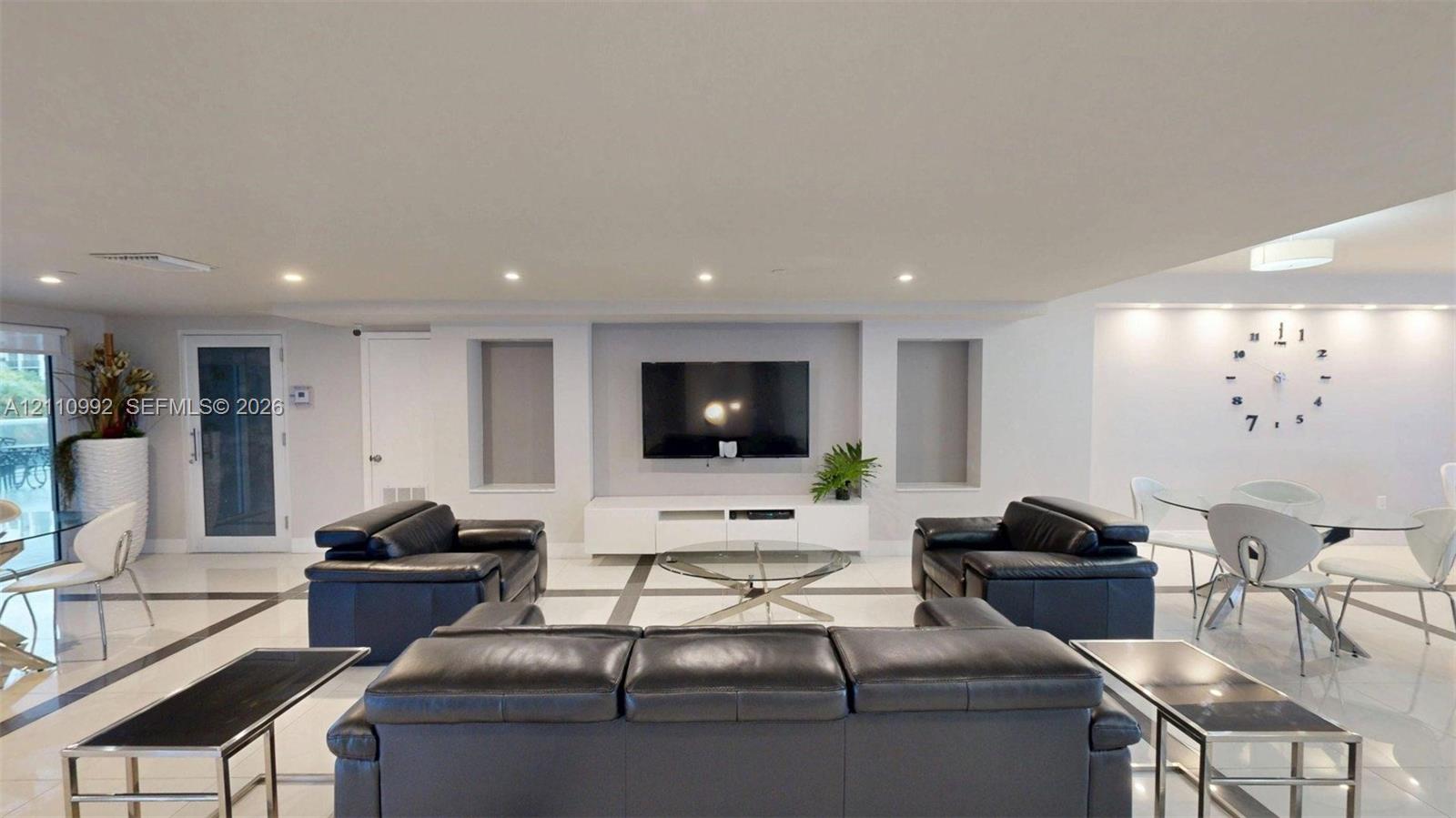 Open-concept living space featuring high-gloss tile flooring, recessed ceiling lighting, a built-in entertainment niche, and wall-mounted task lighting