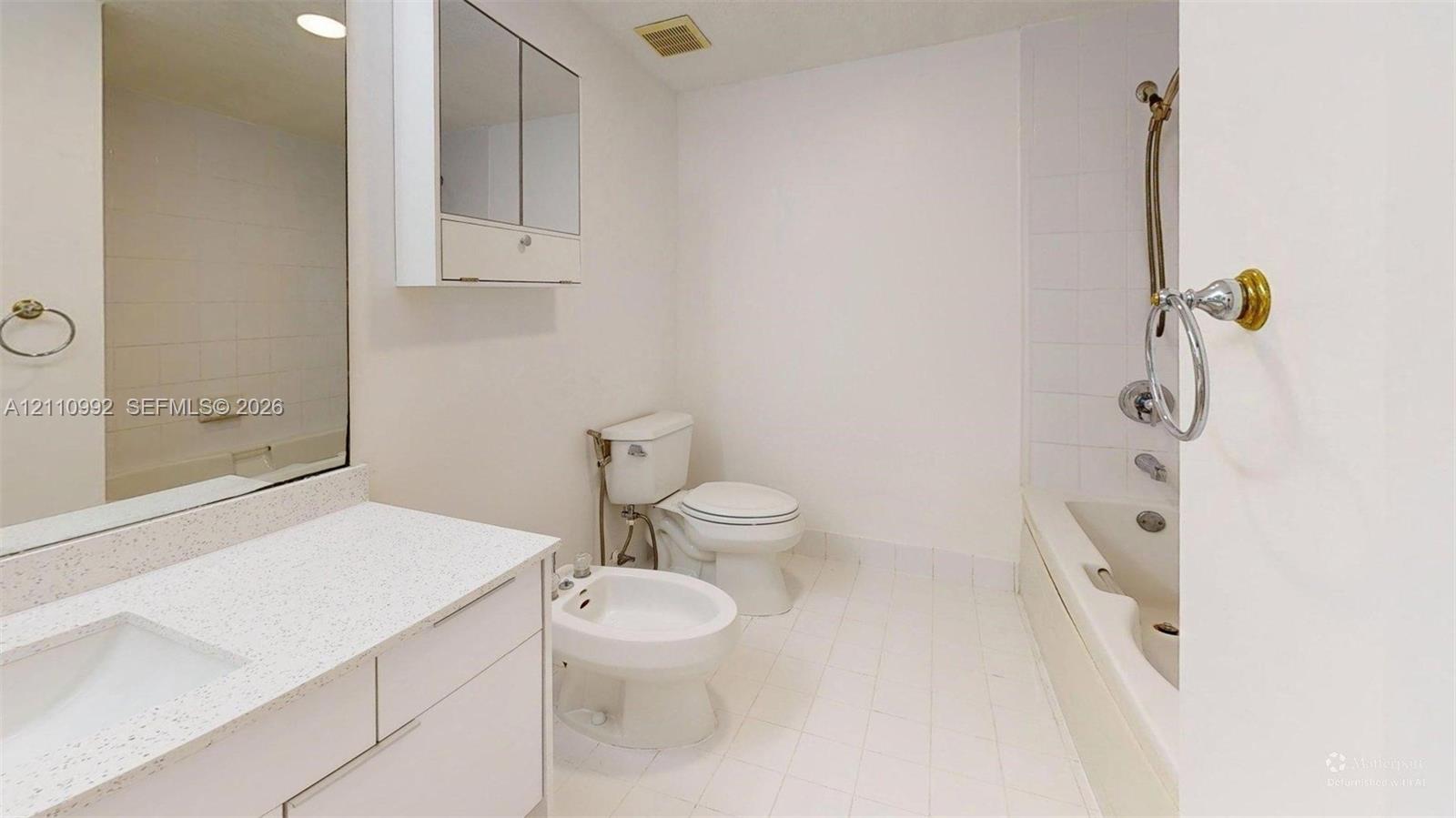 Bathroom featuring a solid-surface countertop with an integrated basin, a wall-mounted medicine cabinet with dual mirrored doors, a bathtub with a tiled surround, and a dedicated bidet