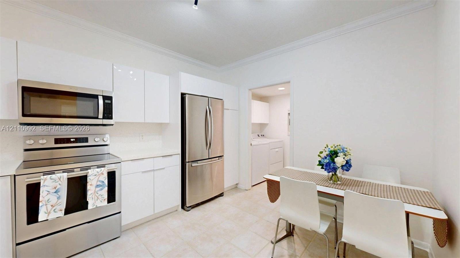 Contemporary kitchen featuring high-gloss white cabinetry, stainless steel appliances, and tile flooring