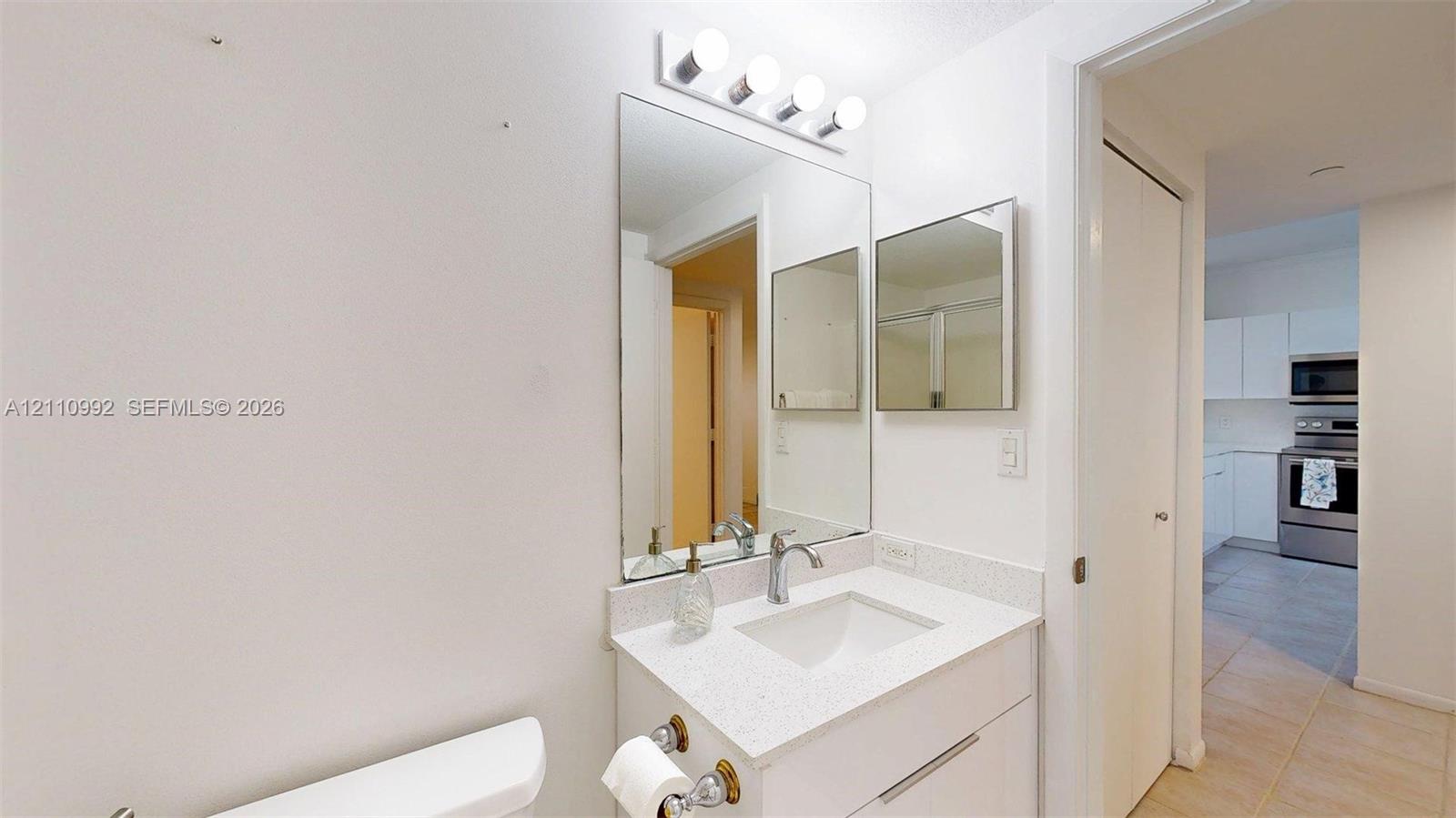 Bathroom vanity featuring a stone-composite countertop, undermount sink, chrome faucet, full-height wall mirror, and integrated lighting