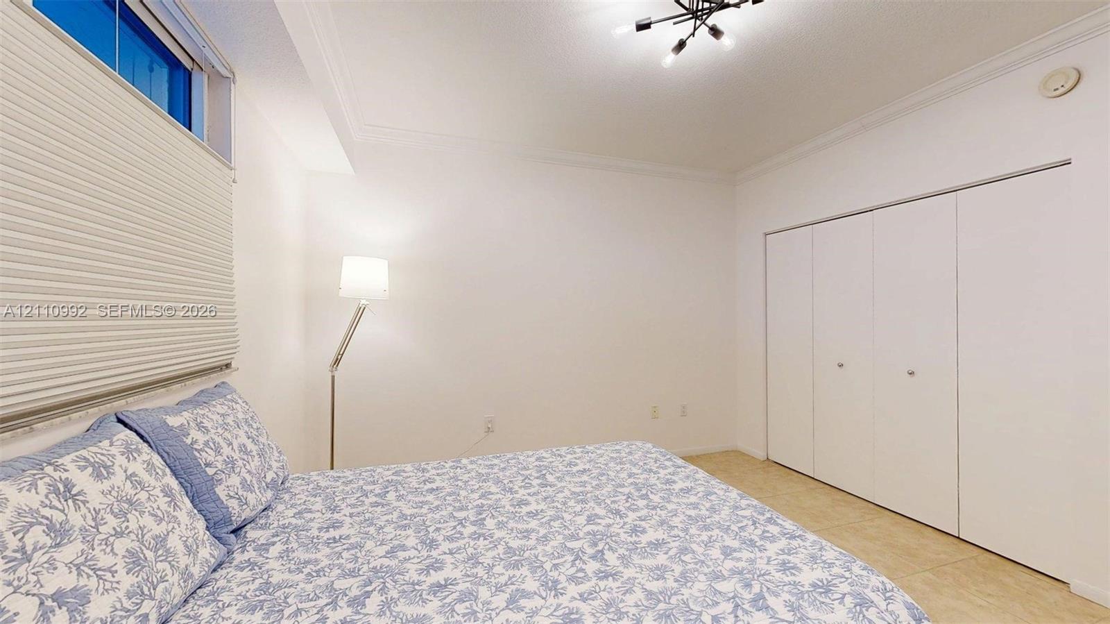 Multi-panel closet with white doors, window with pleated shades, crown molding, and modern geometric ceiling lighting fixture