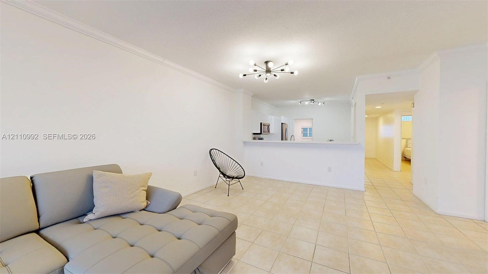 Neutral tile flooring, crown molding, multi-arm flush-mount lighting, and a breakfast bar counter