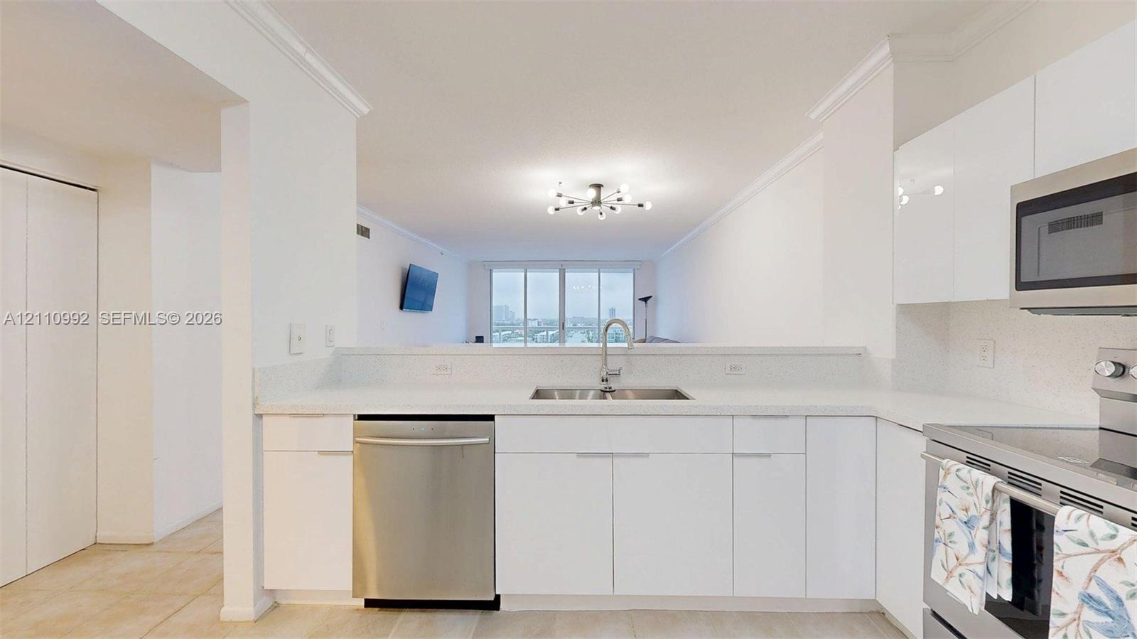 Kitchen featuring white flat-panel cabinetry, light-toned countertops, stainless steel appliances, and a polished chrome faucet with a dual-basin sink