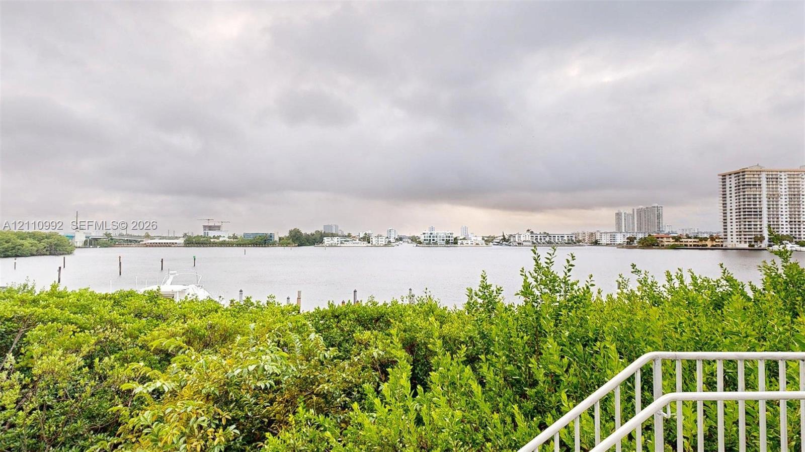 Elevated balcony featuring a white metal railing and a direct outlook over the coastal waterway, mature native vegetation, and the urban skyline