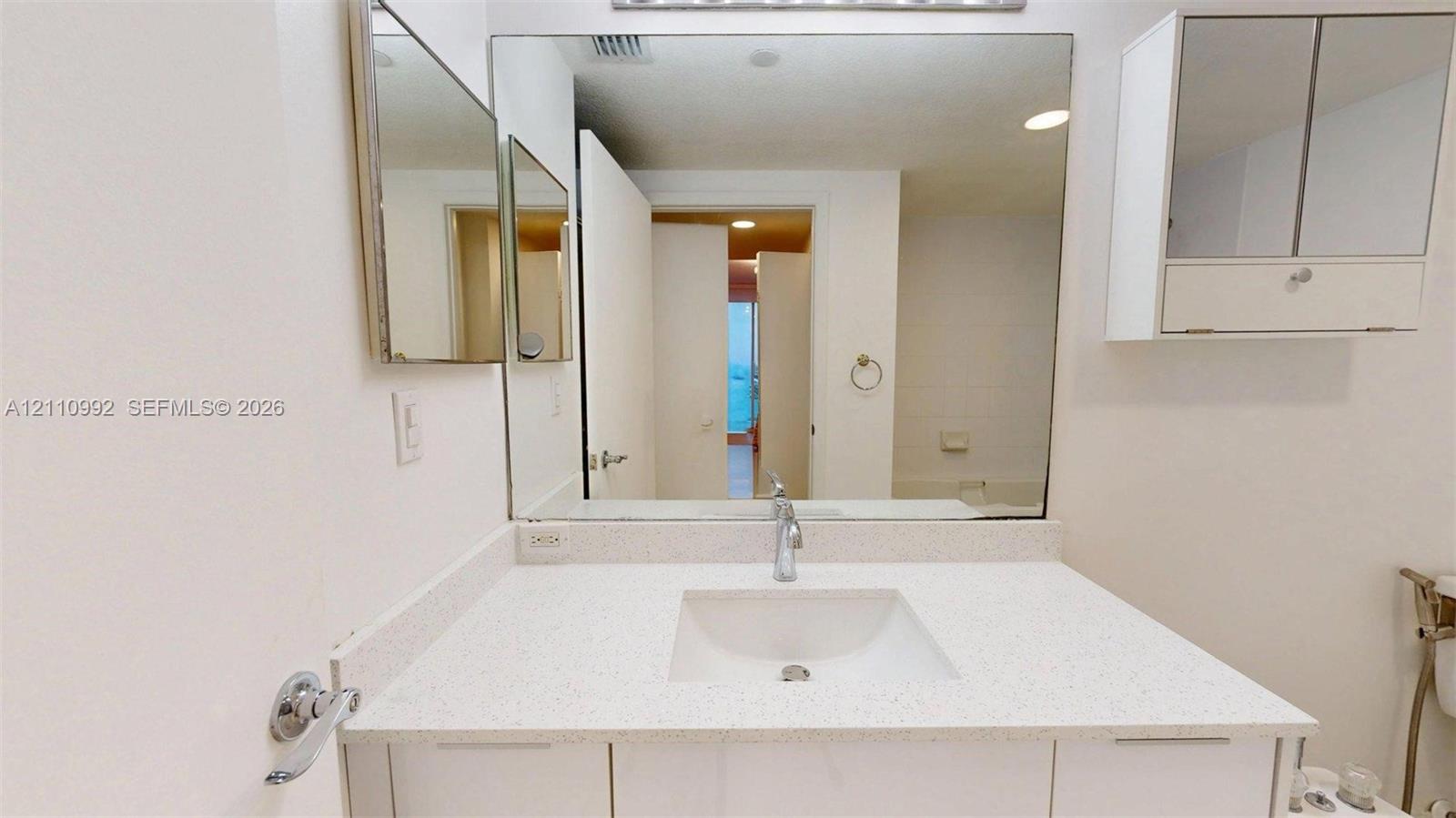 Bathroom vanity featuring a solid surface countertop, integrated sink, chrome faucet, wall-mounted medicine cabinet, and large frameless mirror