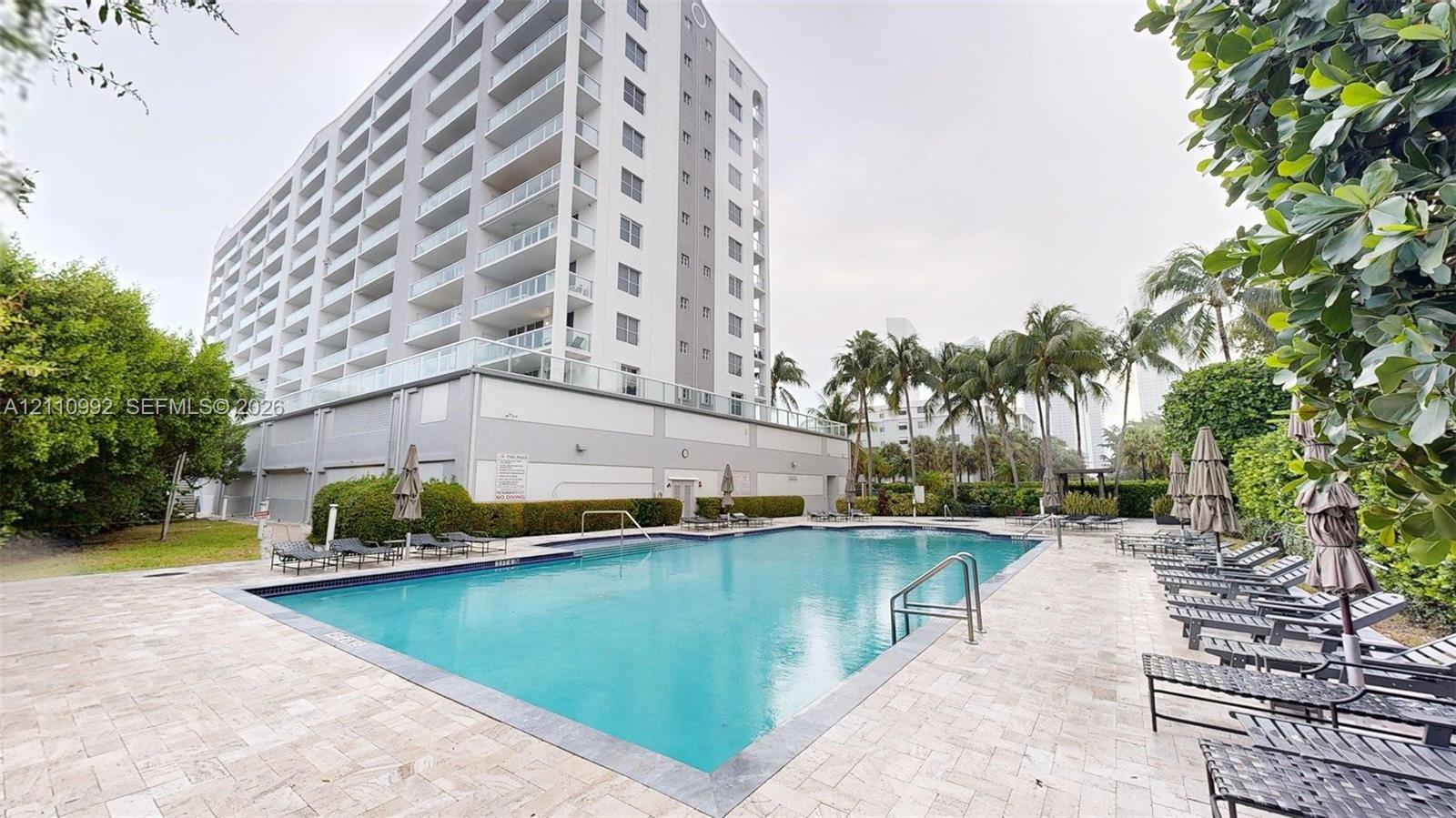 In-ground swimming pool featuring stone tile decking, metal handrails, and surrounding mature landscaping