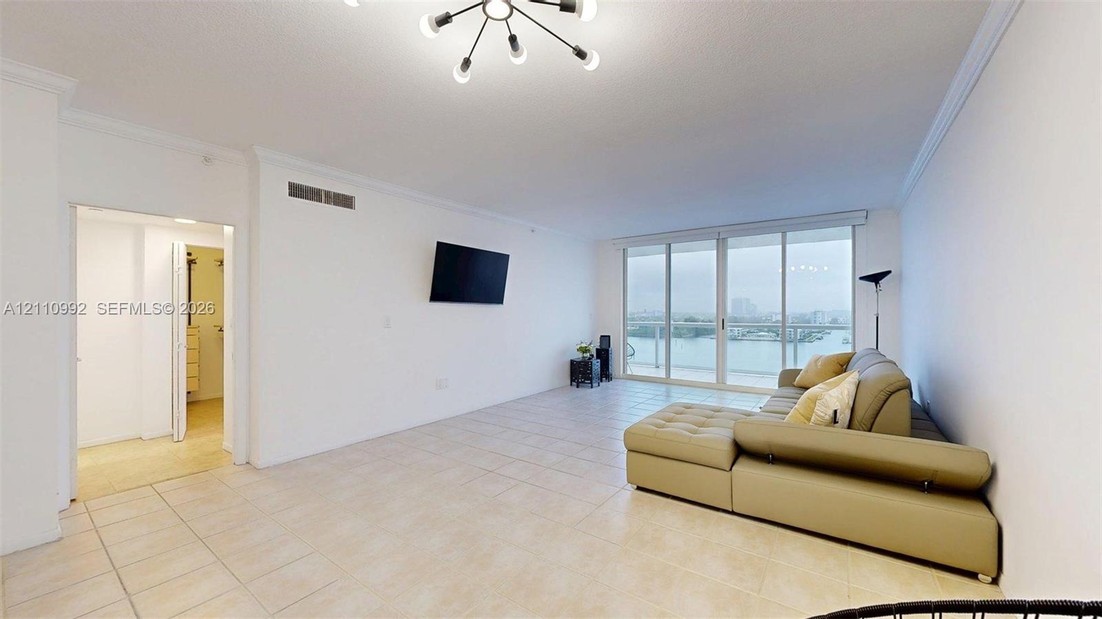 Open-concept living space featuring large-format tile flooring, a multi-arm modern ceiling light fixture, expansive floor-to-ceiling glass sliding doors, and a private balcony